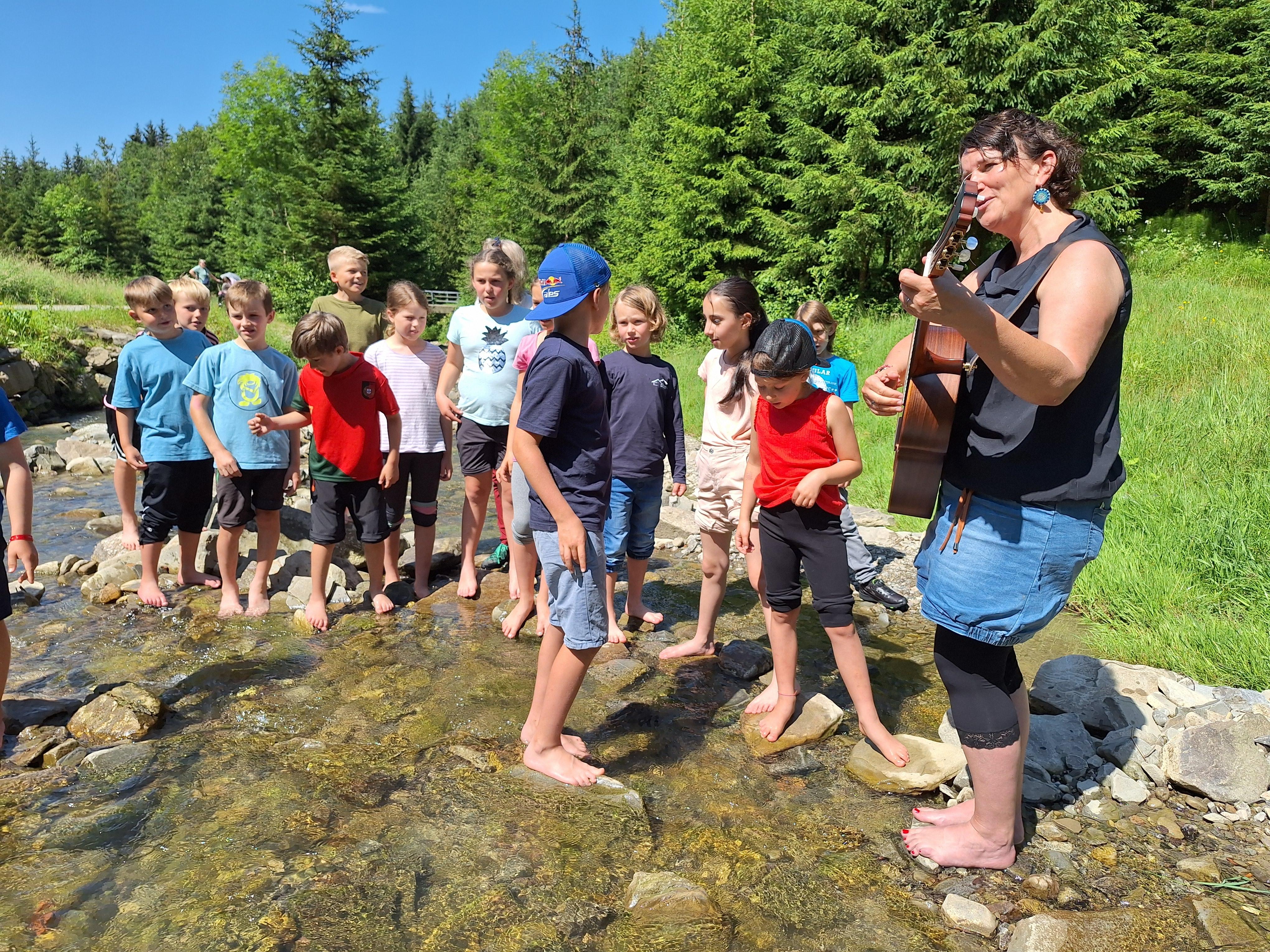 Die Schulkinder aus Rettenbach haben eine besondere Unterrichtsstunde: Gemeinsam mit der Allgäuer Künstlerin Hedwig Roth stehen sie im Galetschbach und jodeln.