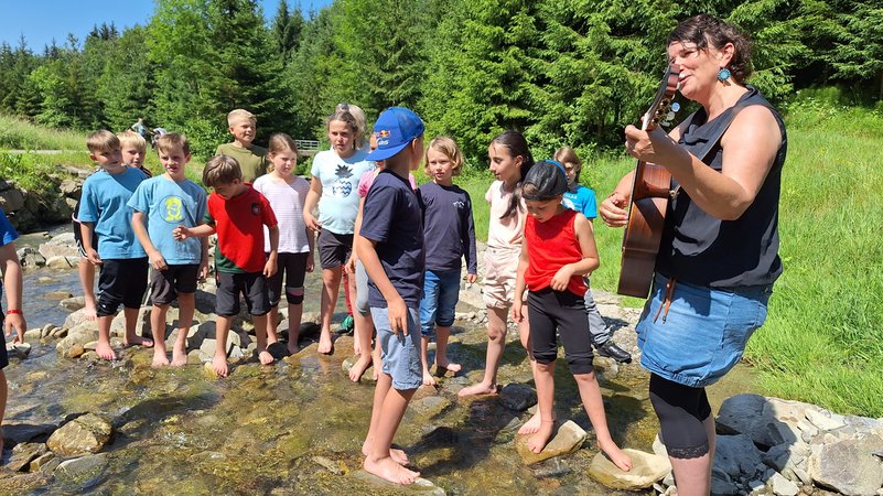 Die Schulkinder aus Rettenbach haben eine besondere Unterrichtsstunde: Gemeinsam mit der Allgäuer Künstlerin Hedwig Roth stehen sie im Galetschbach und jodeln. | Bild: BR/Brigitte Kornberger Die Schulkinder aus Rettenbach haben eine besondere Unterrichtsstunde: Gemeinsam mit der Allgäuer Künstlerin Hedwig Roth stehen sie im Galetschbach und jodeln.