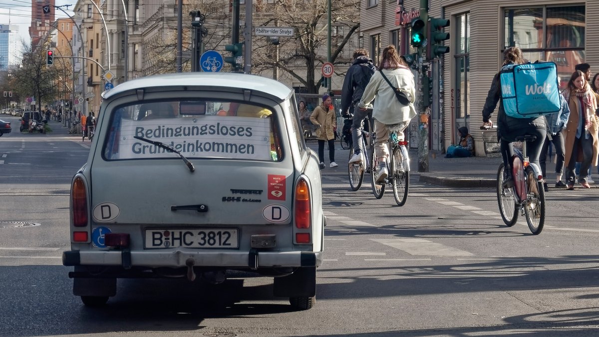 Trabi mit Schild "Bedingungsloses Grundeinkommen", Fahrradfahrer