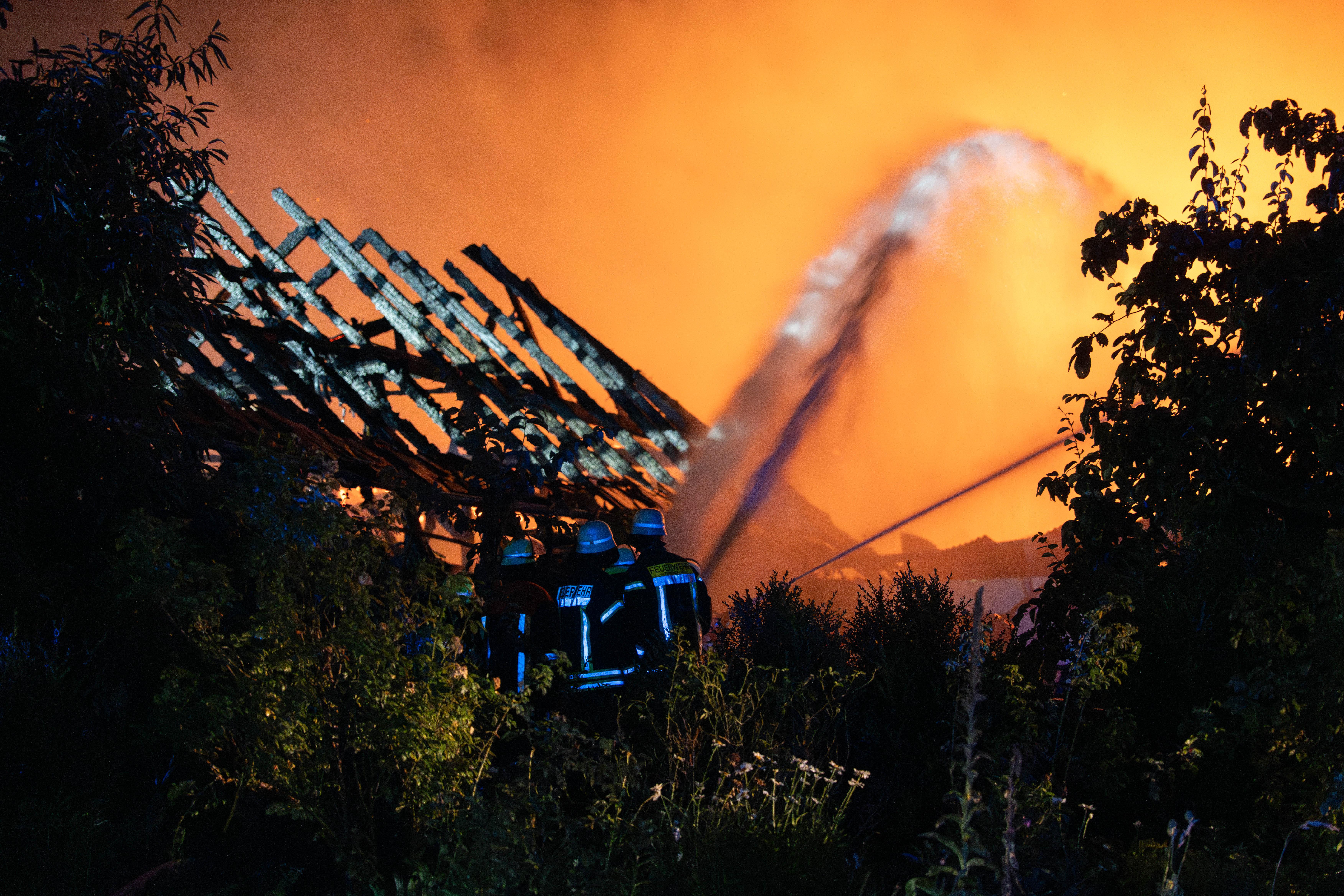 Feuerwehrleute bei Löscharbeiten. Ausgebranntes Gebäude im Hintergrund.