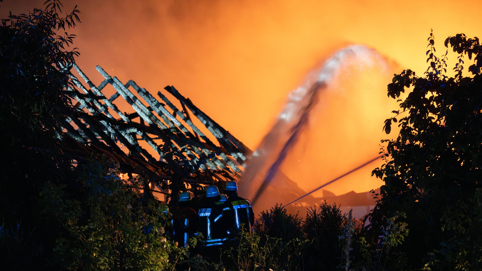 Feuerwehrleute bei Löscharbeiten. Ausgebranntes Gebäude im Hintergrund.