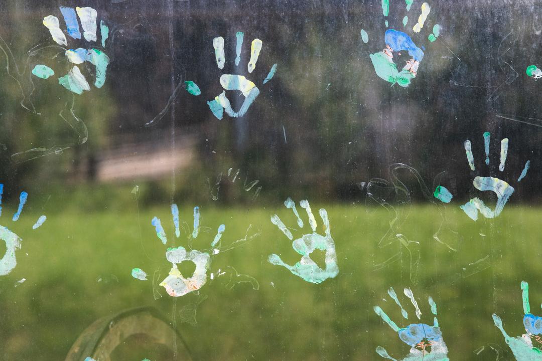 Bunte Handabdrücke aus Fingerfarben auf einer dreckigen Glasscheibe.