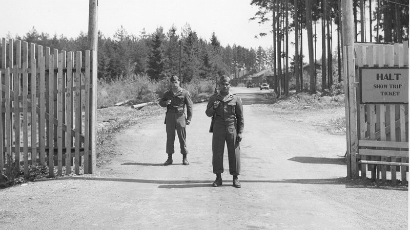Zwei US-Soldaten bewachen den Eingang der Heeresmunitionsanstalt St. Georgen (MUNA). Sie stehen am Tor. Ein Schild zeigt "HALT, show trip ticket". | Bild: isdcw.org Zwei US-Soldaten bewachen den Eingang der Heeresmunitionsanstalt St. Georgen (MUNA). Sie stehen am Tor. Ein Schild zeigt "HALT, show trip ticket".
