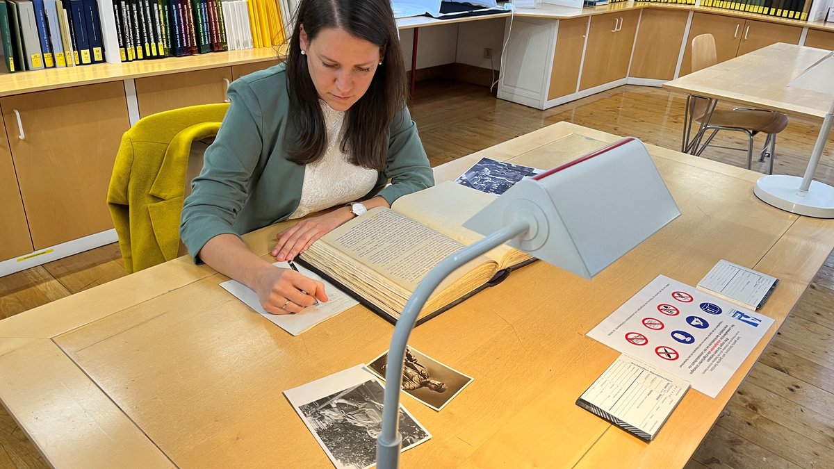 Die Historikerin Eva Karl sitzt an einem Schreibtisch mit zeitgeschichtlichen Dokumenten. 
