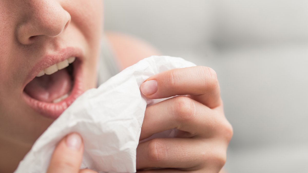 Gesicht einer Frau (Nase und Mund), die in ein Taschentuch niesen wird