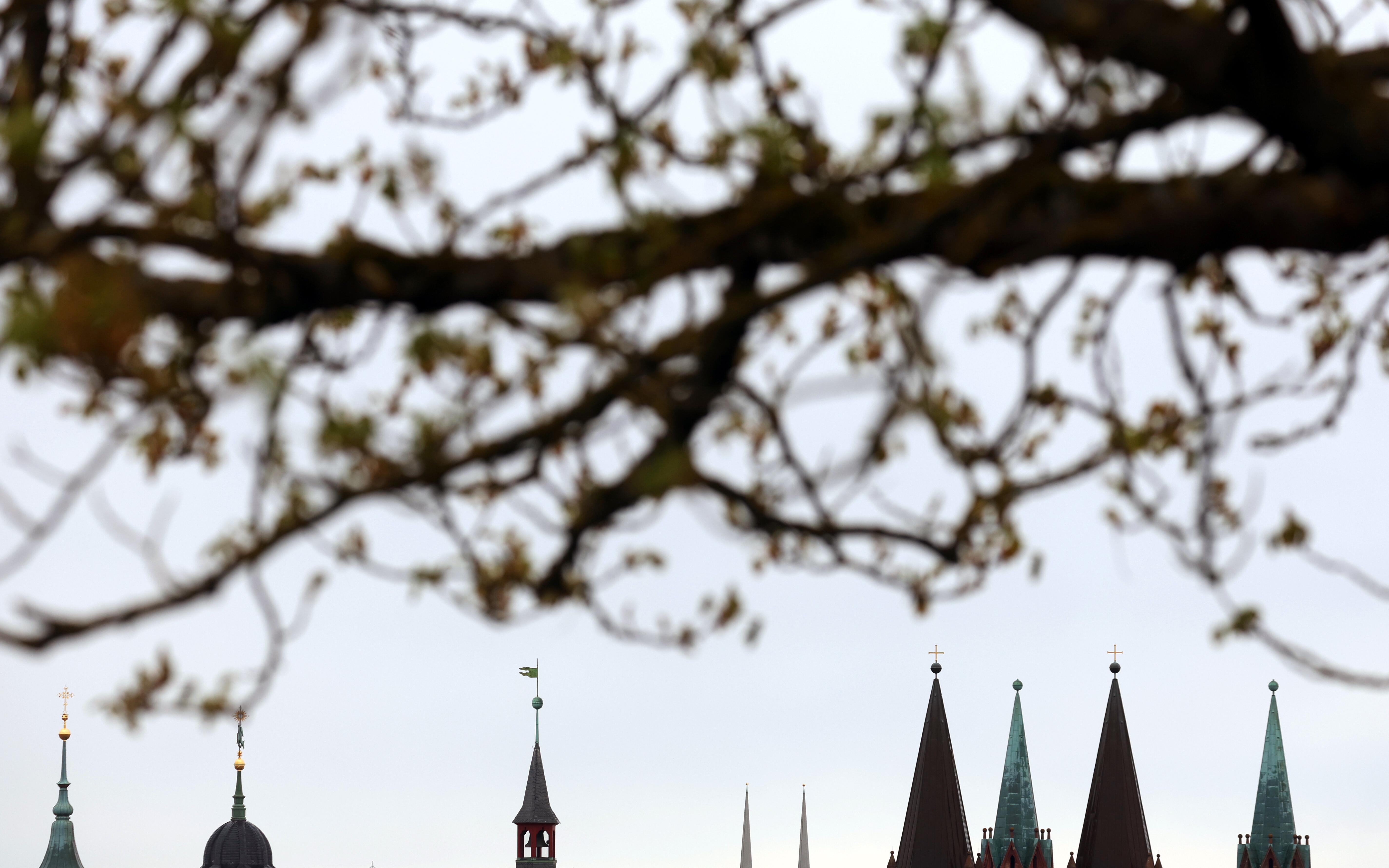 Verschiedene Kirchtürme und der Turm des Rathauses zeichnen sich vor dem bewölktem Himmel in Würzburg ab.