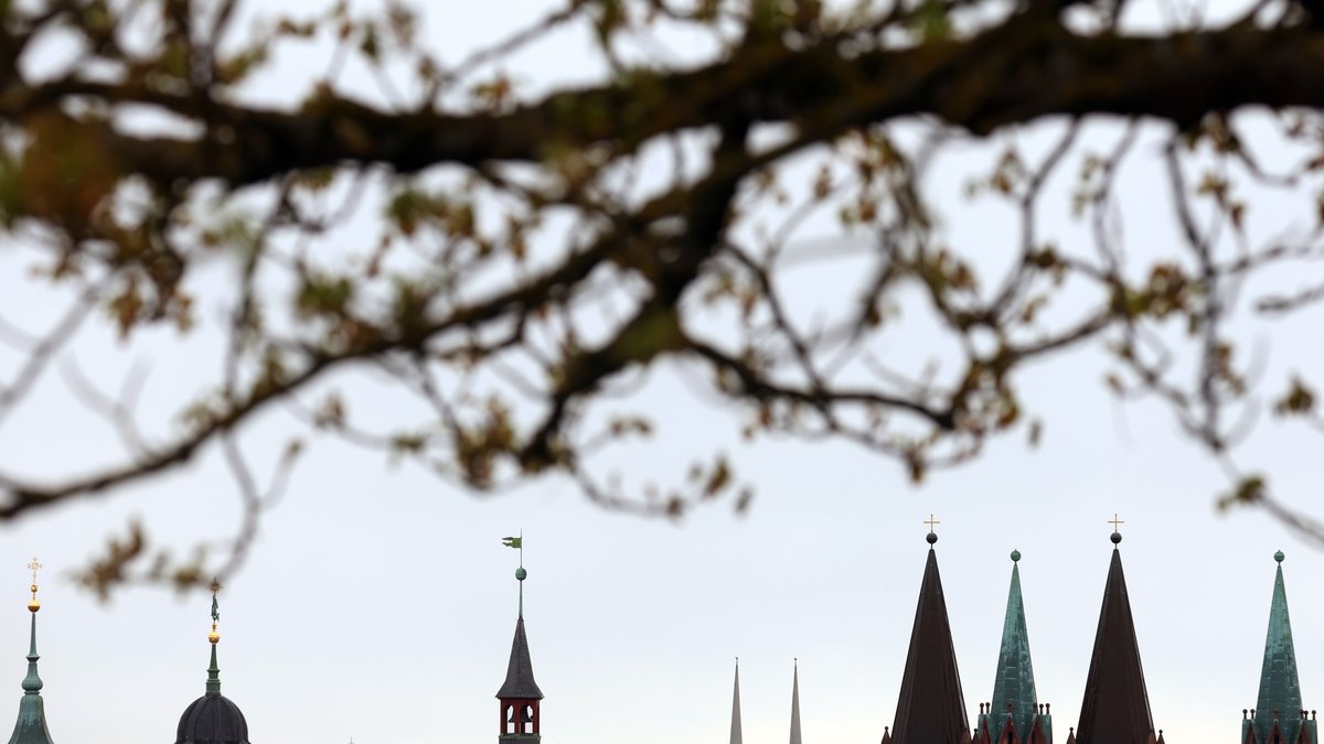 Verschiedene Kirchtürme und der Turm des Rathauses zeichnen sich vor dem bewölktem Himmel in Würzburg ab.