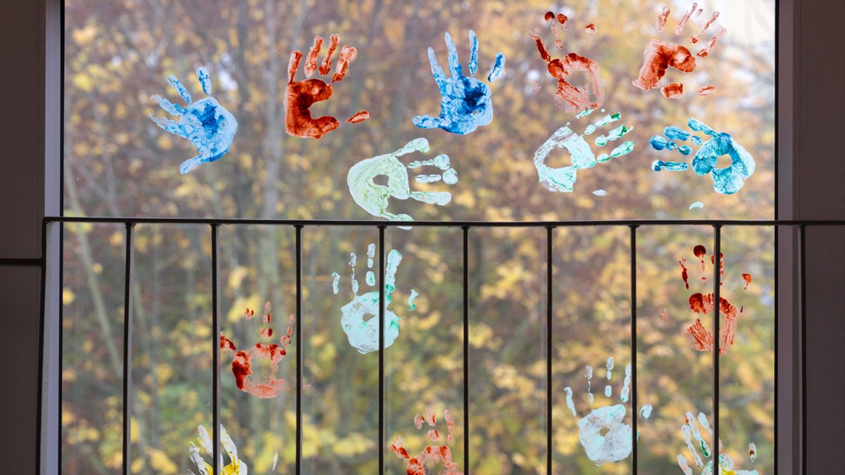 Kinder haben in einem Kindergarten farbige Abdrücke ihrer Hände auf einem Fenster hinterlassen.