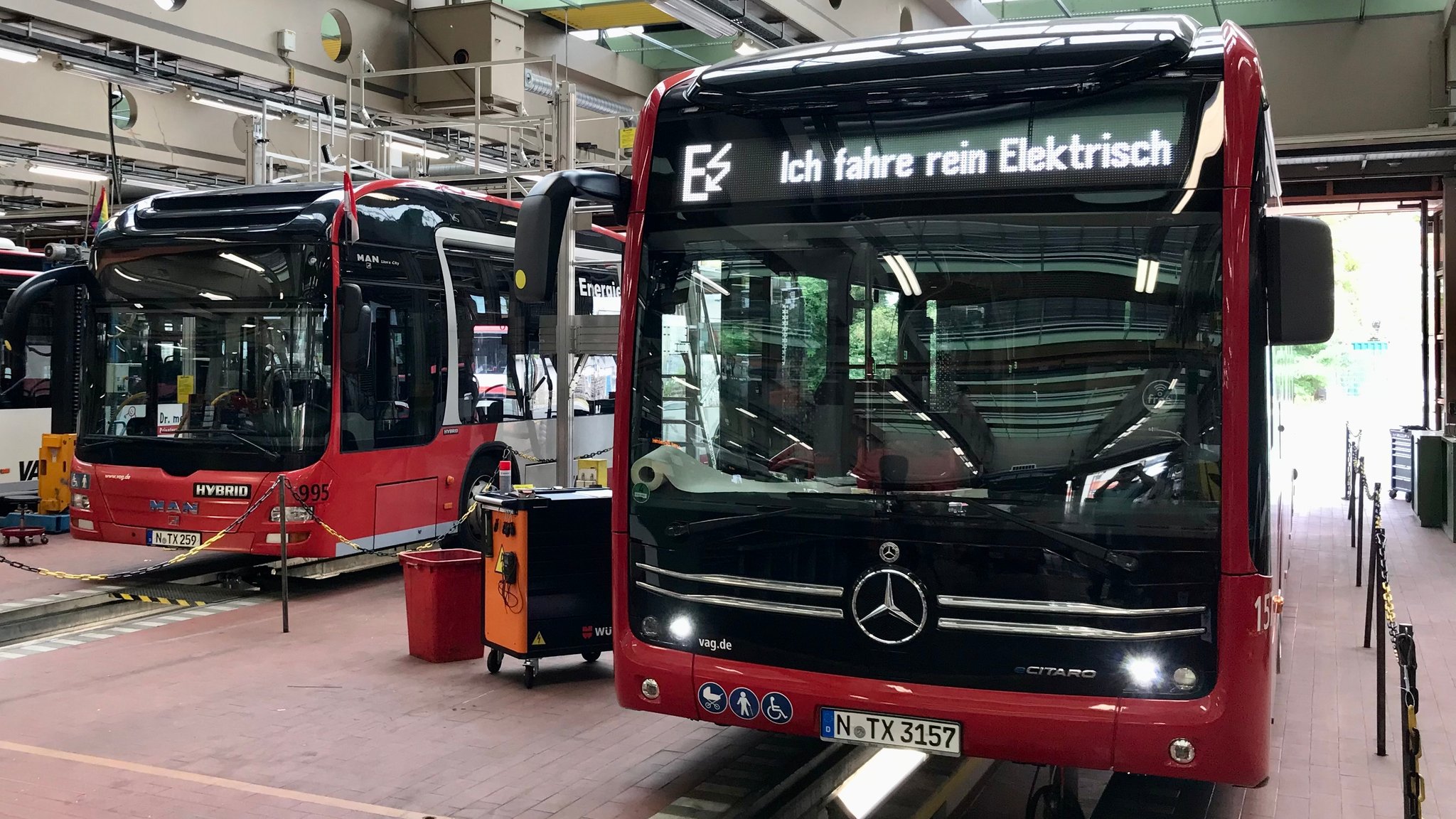 Busse in einem Depot, bei einem steht auf dem Spruchband "Ich fahre rein elektrisch"