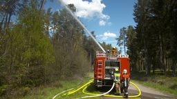 Ein Feuerwehrmann spritzt von einem Einsatzfahrzeug aus Wasser in einen Wald | Bild:BR/Laura Nadler