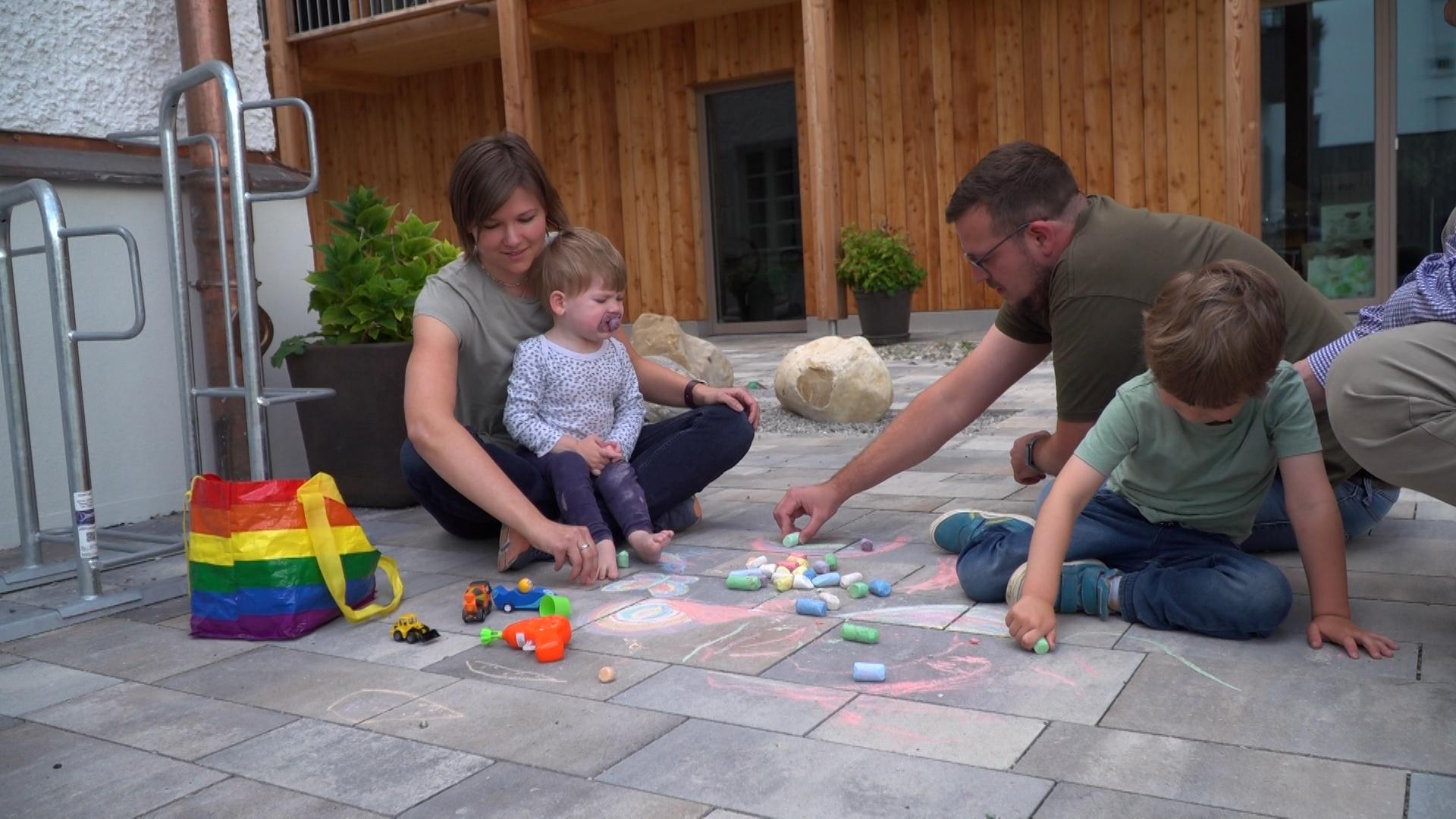 Eine Familie mit zwei Kindern sitzt auf einem Stein-Fußboden im Hof und malt mit Kreide