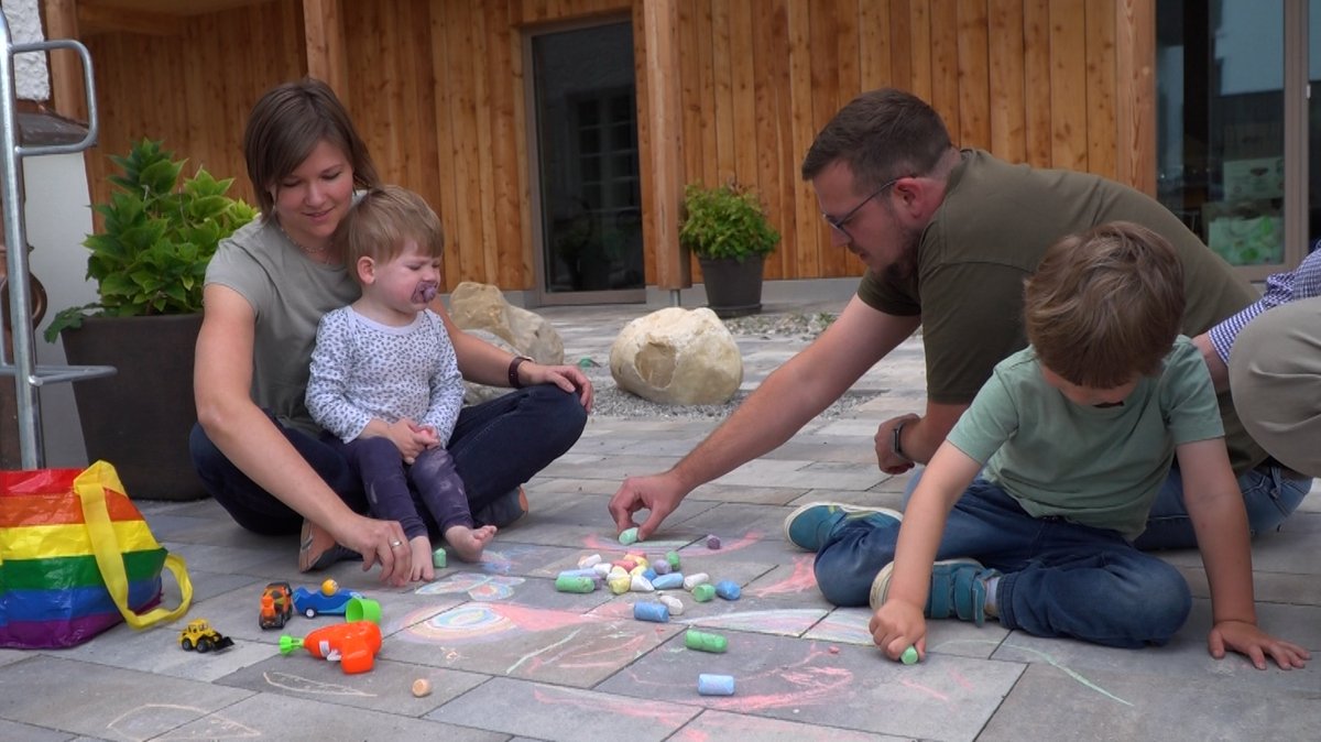 Eine Familie mit zwei Kindern sitzt auf einem Stein-Fußboden im Hof und malt mit Kreide