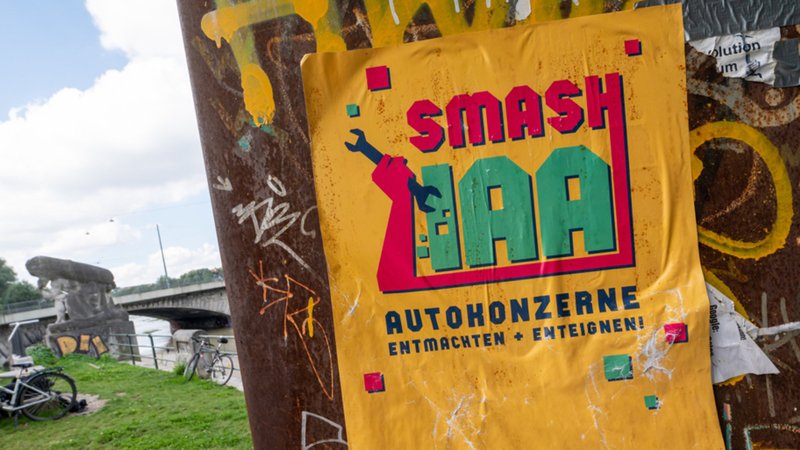 Ein gelbes Plakat mit der Aufschrift "Smash IAA Autokonzerne entmachten und enteignen!" klebt an einer Wand in der Stadt. 