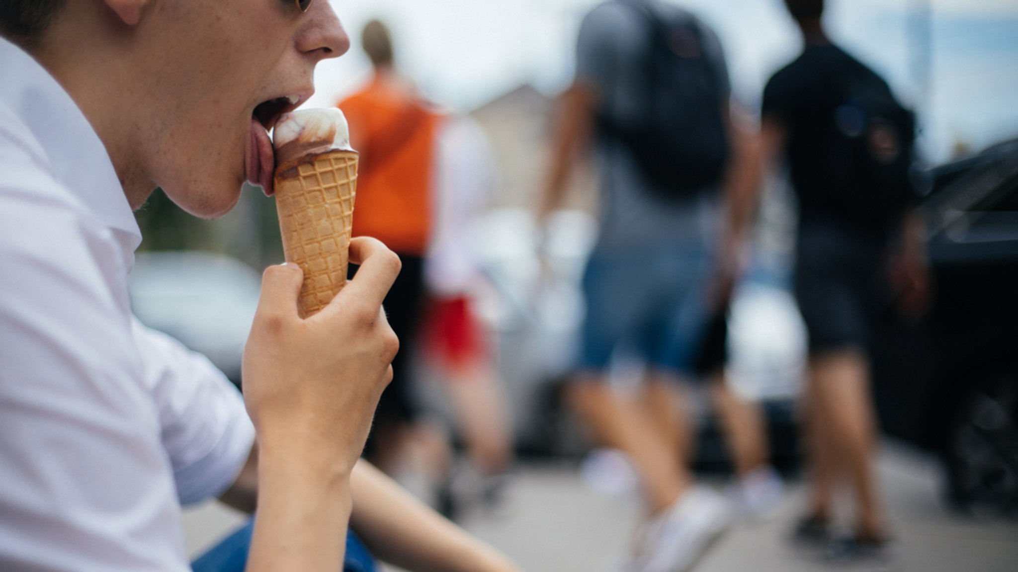 Ein Mann sitzt in einem belebten Umfeld und isst ein Eis.