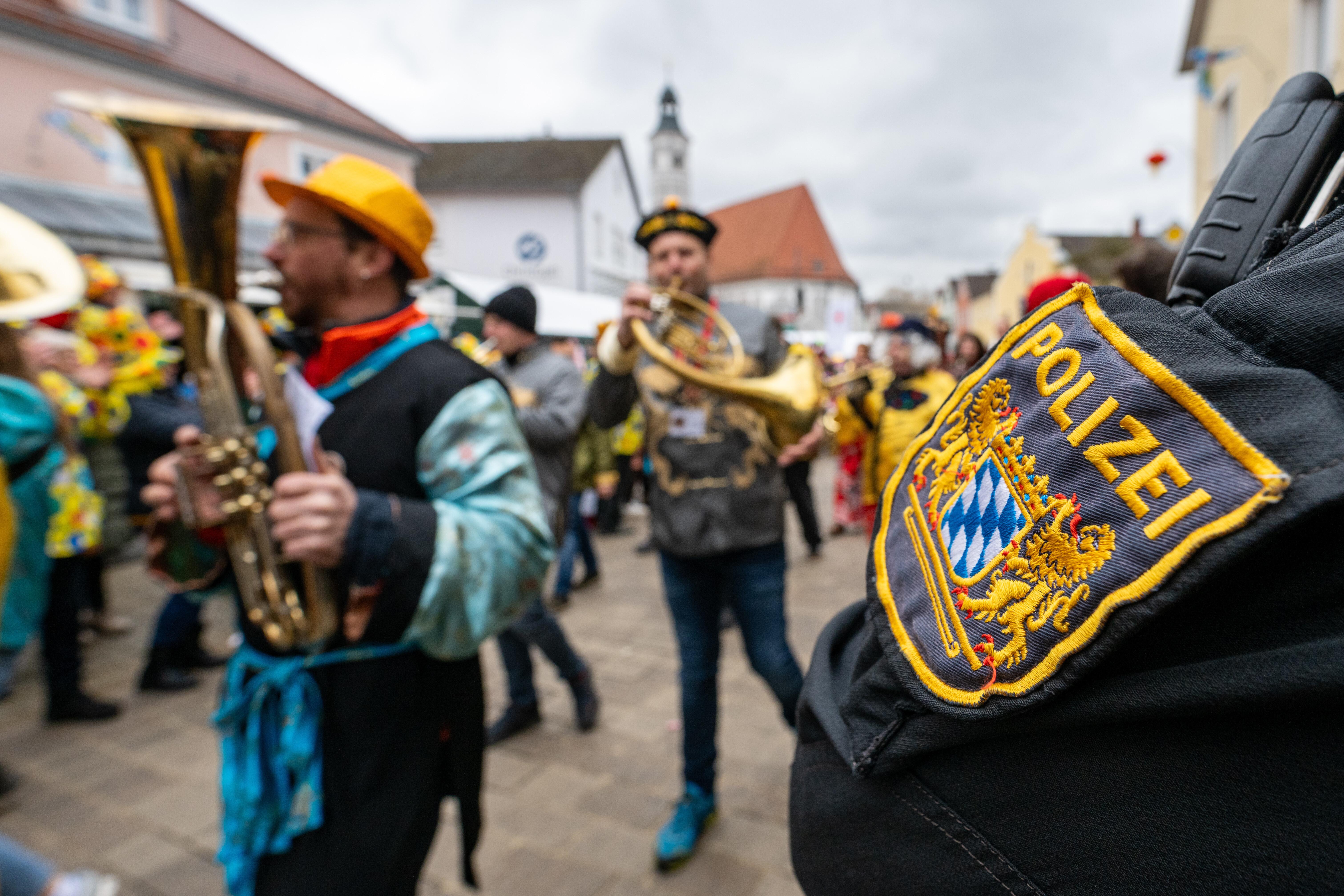 Ein Polizist steht bei einem Faschingszug. An ihm ziehen mehrere Männer mit Musikinstrumenten vorbei. 
