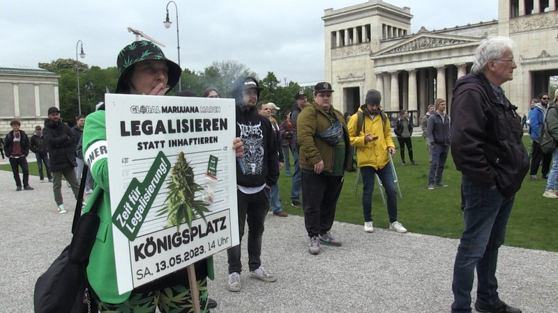 Demonstranten auf dem Münchner Königsplatz, einer hält ein Schild mit der Aufschrift: Legalisieren statt inhaftieren.