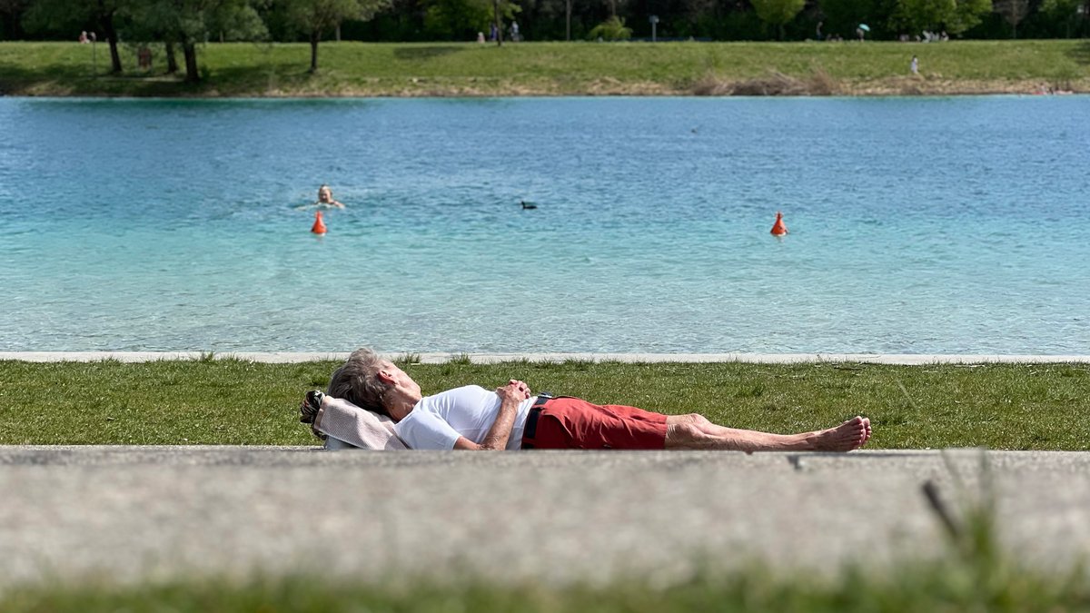Eine Frau liegt bei sonnigem Wetter am Ufer vom Riemer See in München.