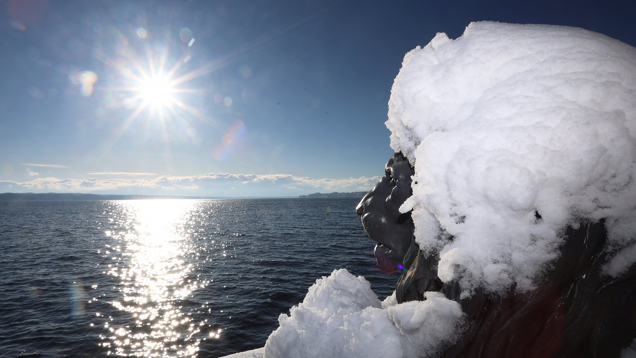 Winter in Tutzing am Starnberger See: Die Löwen-Skulptur am Midgardhaus trägt am Freitag eine Schneehaube und blickt über den See auf die Sonne.