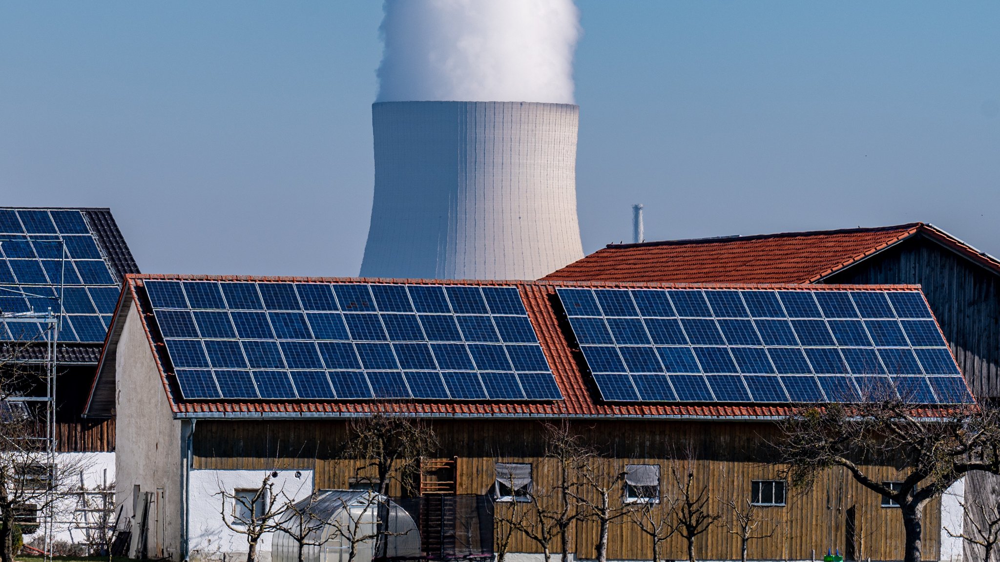 Archivbild: Wasserdampf steigt aus dem Kühlturm vom Atomkraftwerk (AKW) Isar 2. Davor steht ein Stall mit einer Photovoltaikanlage.