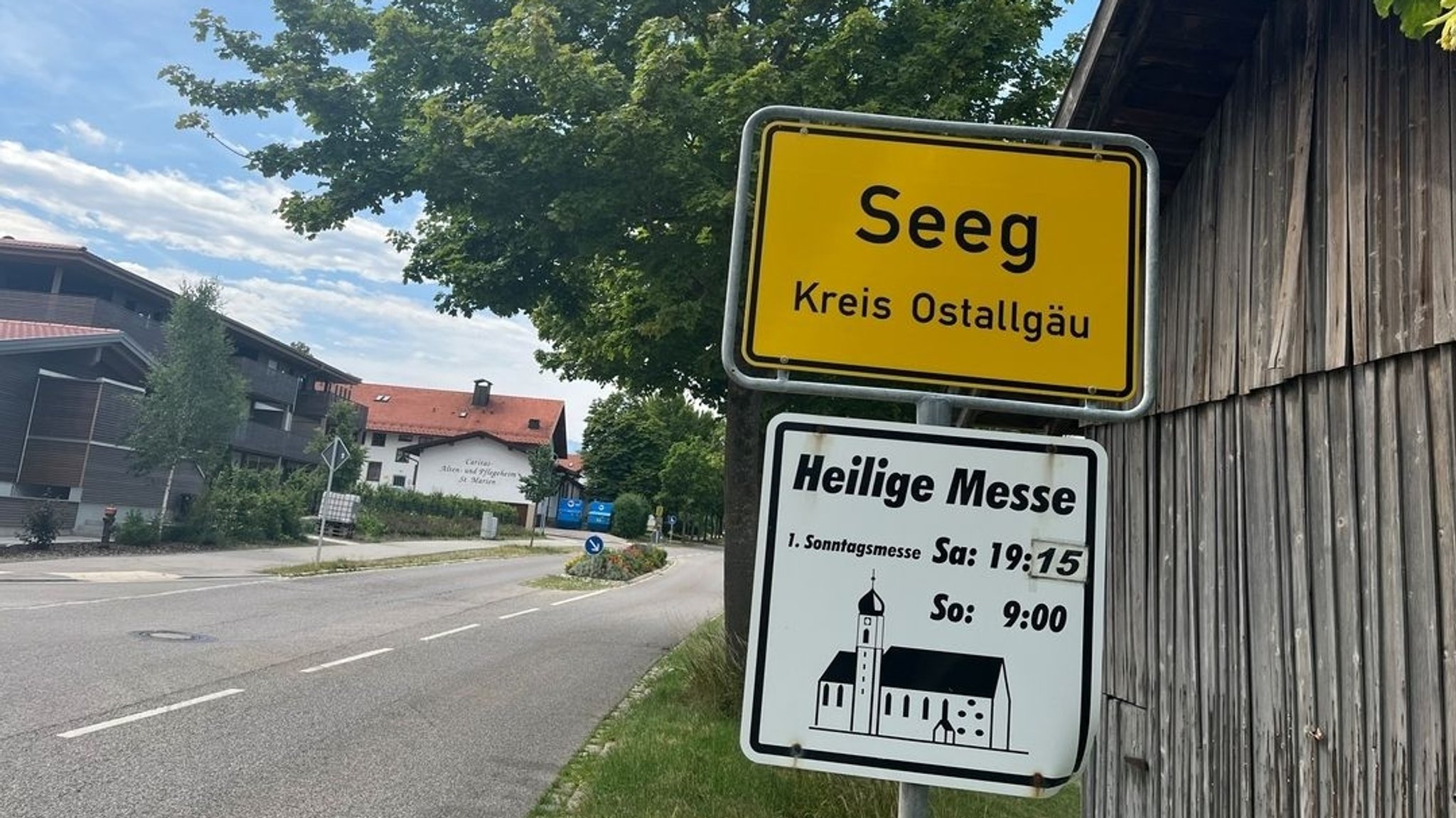 Ein Ortsschild, darunter eine Gottesdiensttafel in Seeg im Ostallgäu