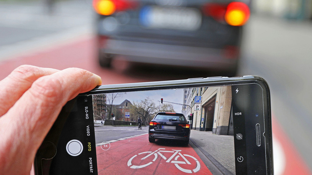 Auf einem Smartphone ist das Bild eines Autos zu sehen, das auf einem Radstreifen hält (Symbolbild).