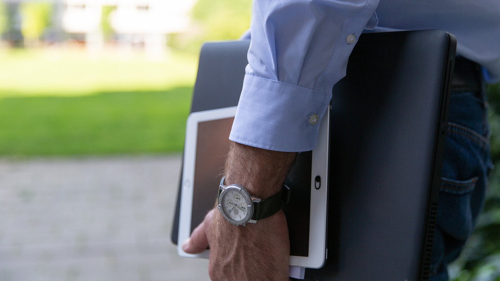 Arm eines Mannes mit Armbanduhr und Laptop/Netbook in der Hand.