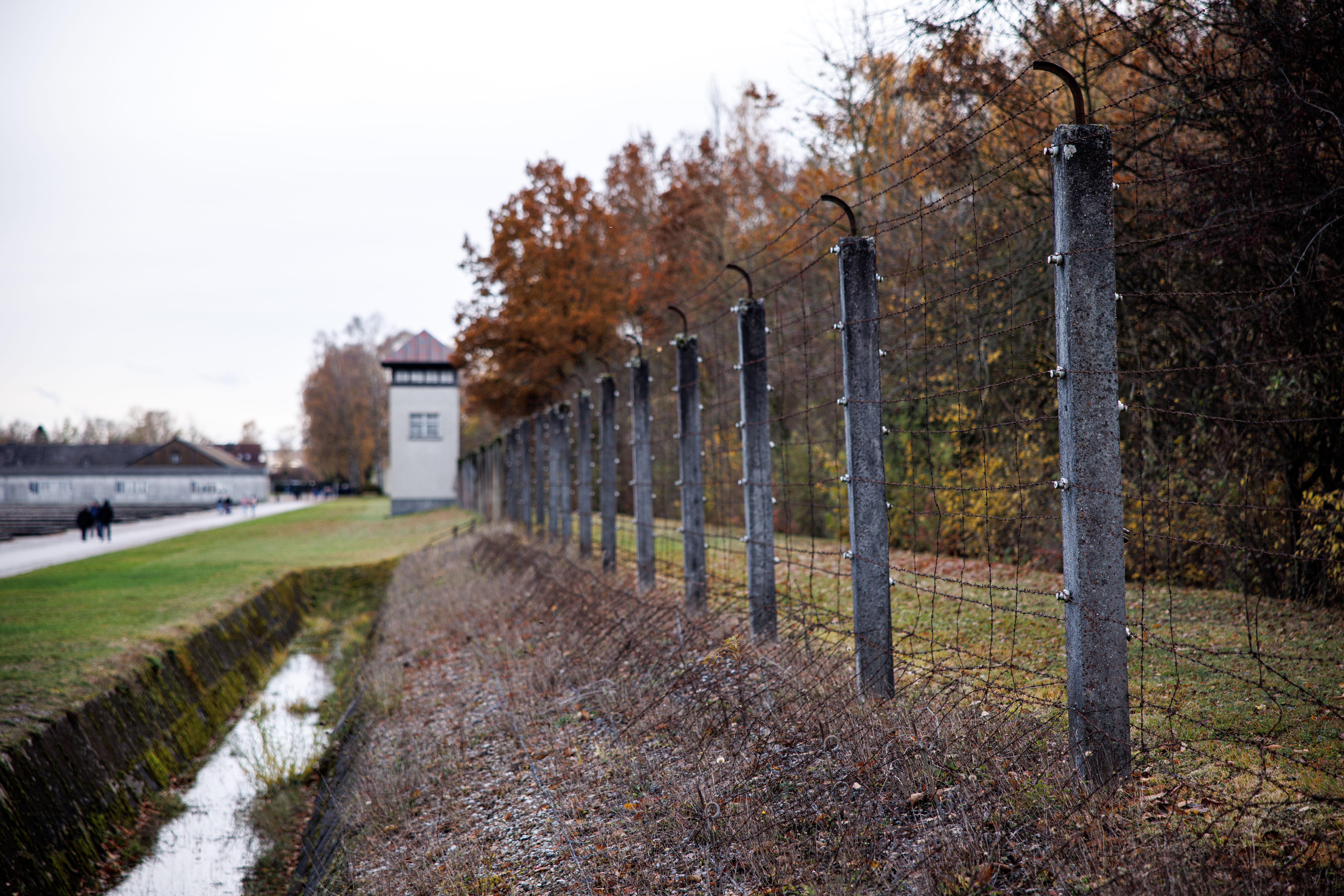 Zaun mit Stacheldraht und Wachturm an einer Kontrollstraße auf dem Gelände der KZ-Gedenkstätte Dachau.