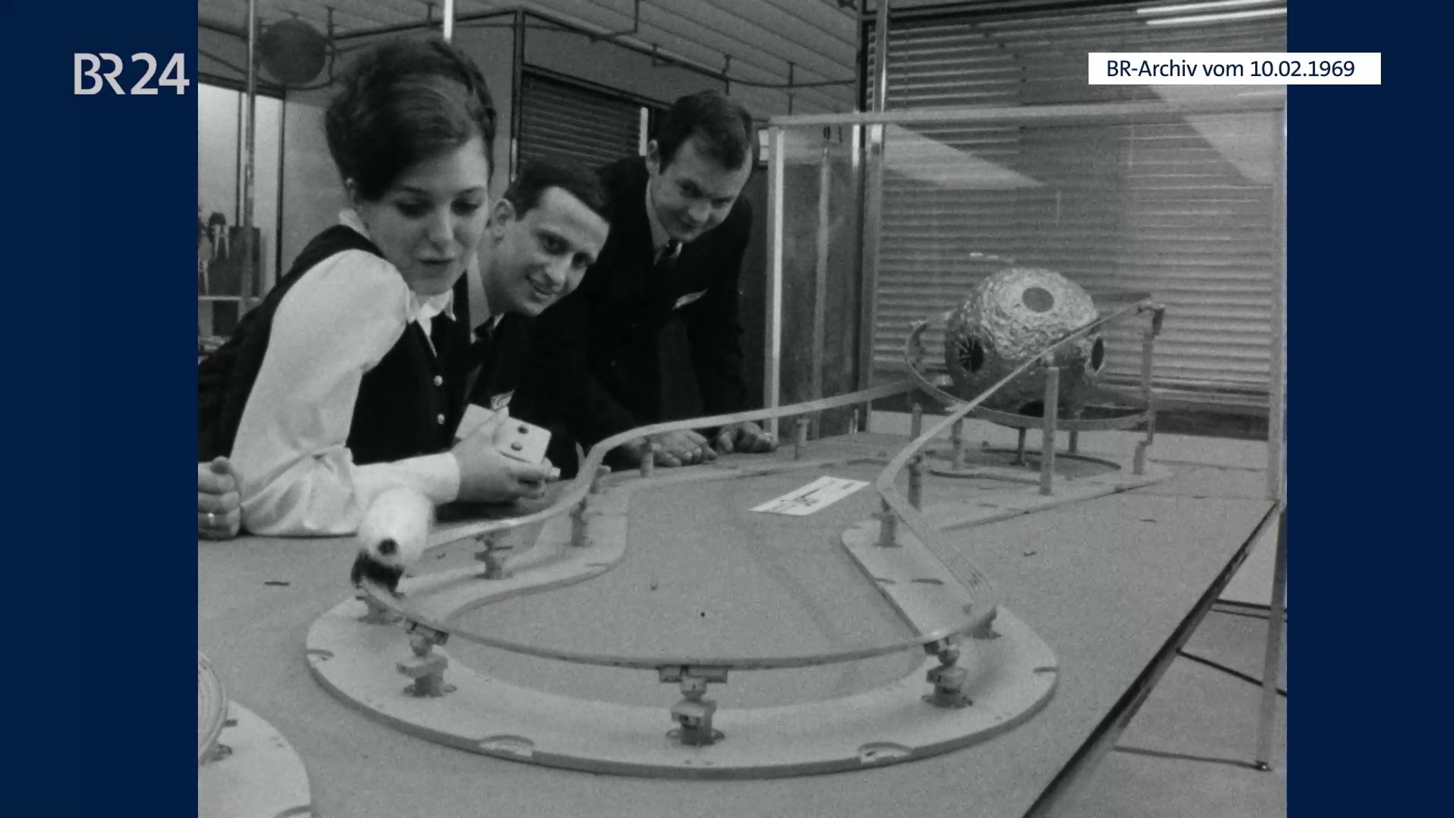 Frau beim Spielen mit der Rennbahn Carrera Jet Apollo. Zwei Männer schauen dabei zu.