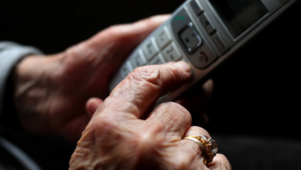 Eine alte Dame hält ein Telefon in der Hand. 