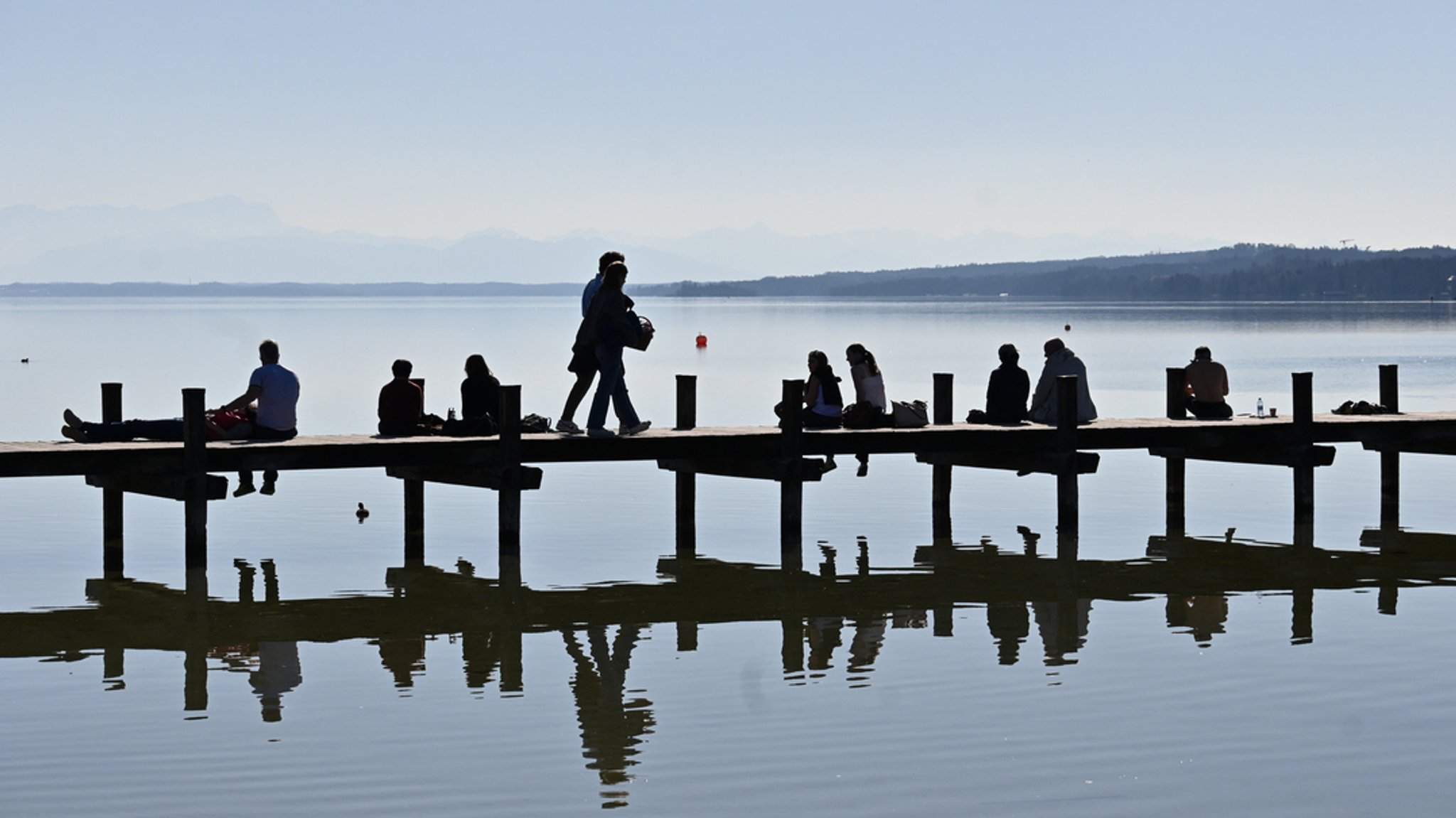 Sonnenanbetende auf einem Steg am Starnberger See im März