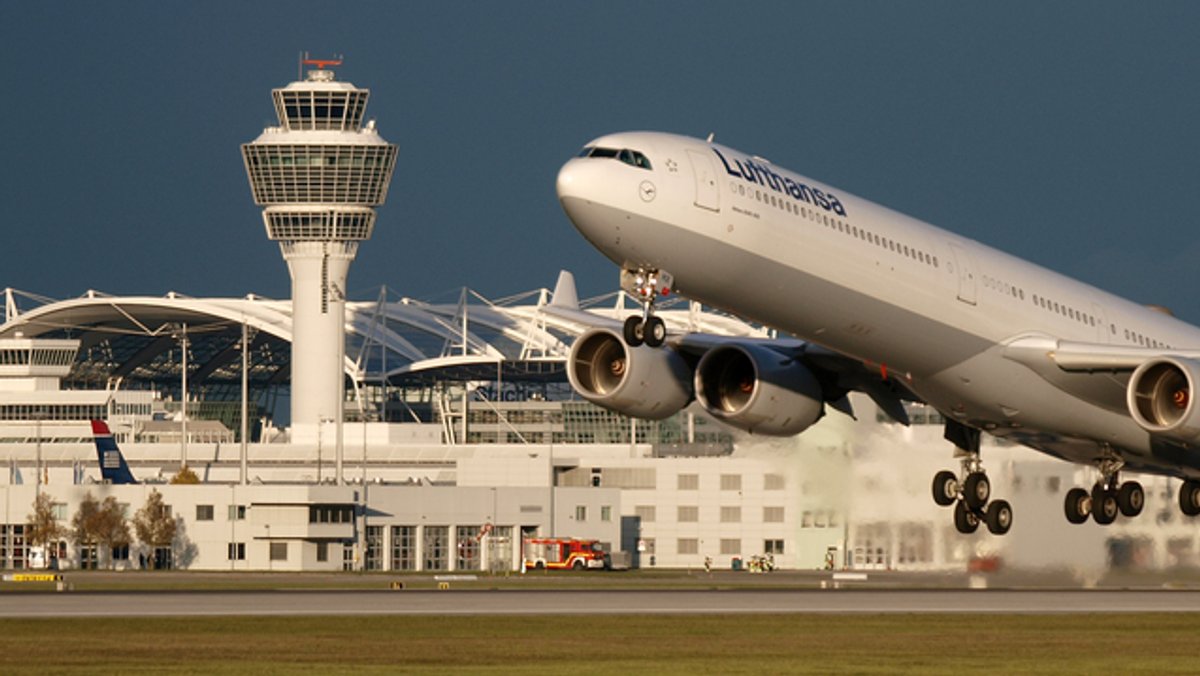 Zu sehen ist der Münchner Flughafen mit einem startenden Lufthansa-Flugzeug im Vordergrund.