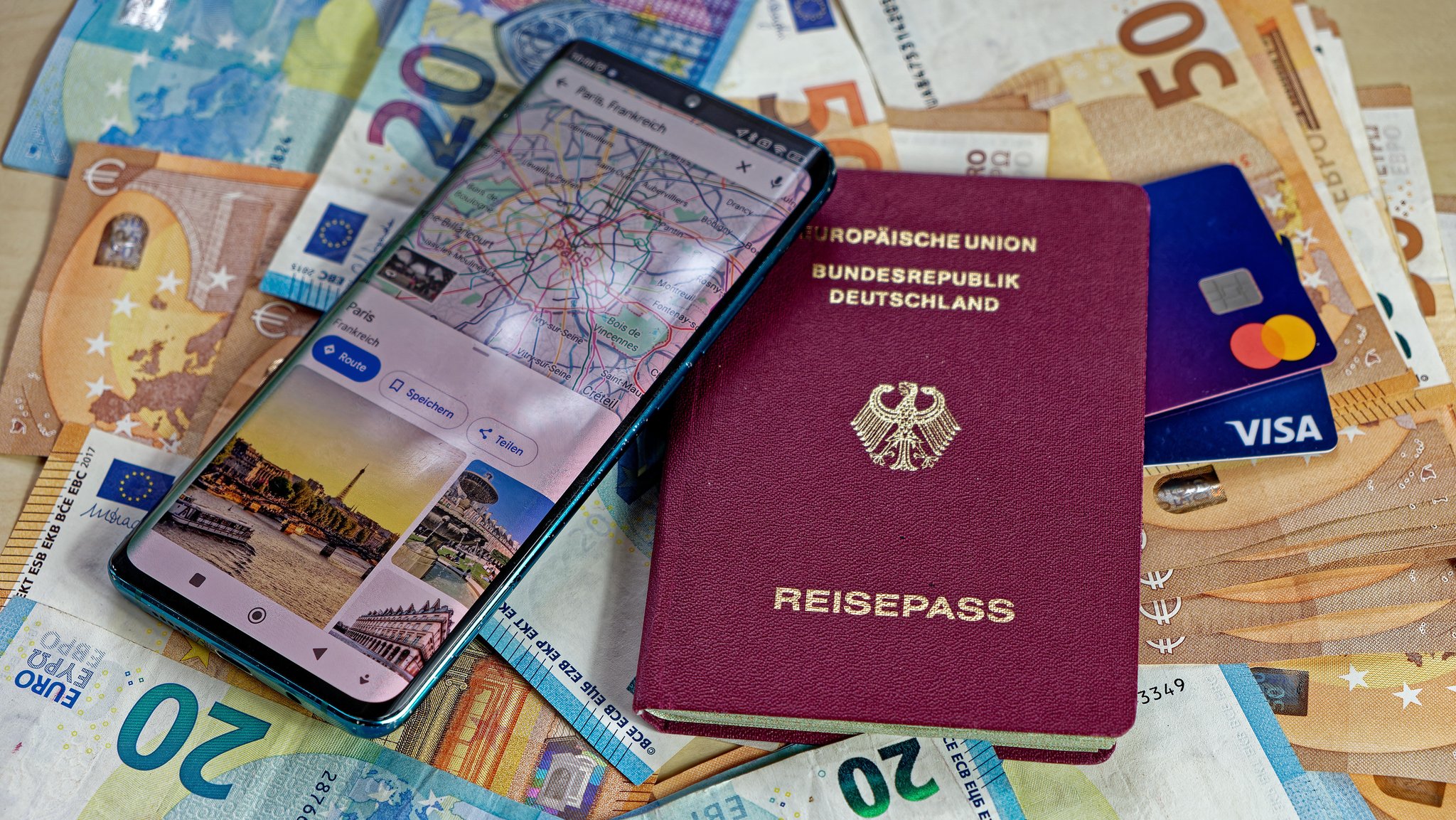 Deutscher Reisepass mit Geldscheinen, Kreditkarten und Smartphone mit App mit Landkarte und Sehenswürdigkeiten