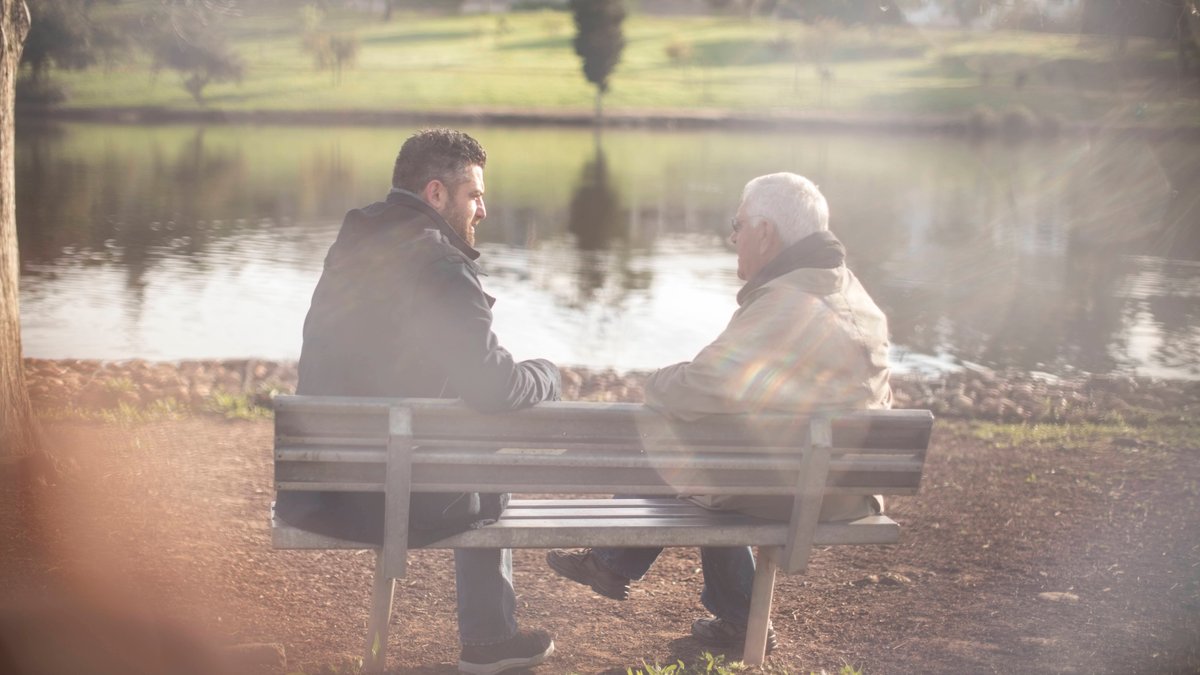 Ein Mann sitzt mit seinem Vater auf einer Parkbank