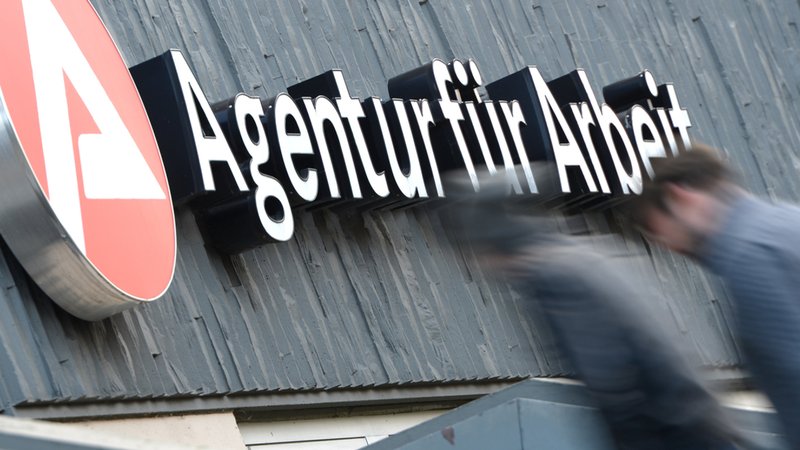 Agentur für Arbeit steht auf einer Häuserfassade. Im Vordergrund sind zwei Männer zu sehen, die sich in Bewegung befinden. | Bild: dpa-Bildfunk/Arne Dedert Agentur für Arbeit steht auf einer Häuserfassade. Im Vordergrund sind zwei Männer zu sehen, die sich in Bewegung befinden.