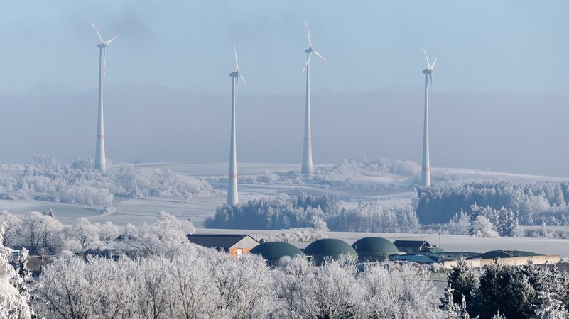 Archivbild: Windkraftanlagen sind am 31.12.2024 nahe der Stadt Hof (Bayern) zu sehen, während im Vordergrund eine Biogasanlage zu sehen ist. | Bild: picture alliance / dpa | Matthias Balk Archivbild: Windkraftanlagen sind am 31.12.2024 nahe der Stadt Hof (Bayern) zu sehen, während im Vordergrund eine Biogasanlage zu sehen ist.