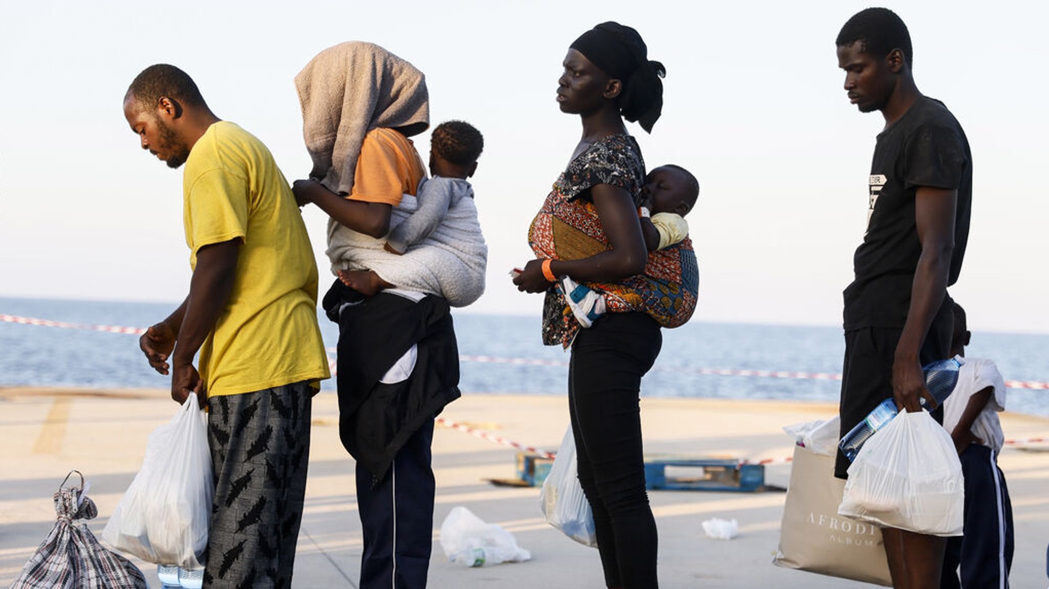 15.09.2023, Italien, Lampendusa: Migranten warten darauf, von der Insel Lampedusa auf ein Schiff zum italienischen Festland gebracht zu werden. Nach der Ankunft Tausender Bootsmigranten seit Wochenbeginn hat sich am Freitag die Situation auf der italienischen Mittelmeerinsel Lampedusa laut Rotem Kreuz entspannt. Am Morgen verließen rund 700 Bootsmigranten die kleine Insel mit Fähren und Polizeischiffen in Richtung Sizilien und Festland. Im Laufe des Tages sollen weitere 2500 Menschen von der Insel gebracht werden. Foto: Cecilia Fabiano/LaPresse via ZUMA Press/dpa +++ dpa-Bildfunk +++