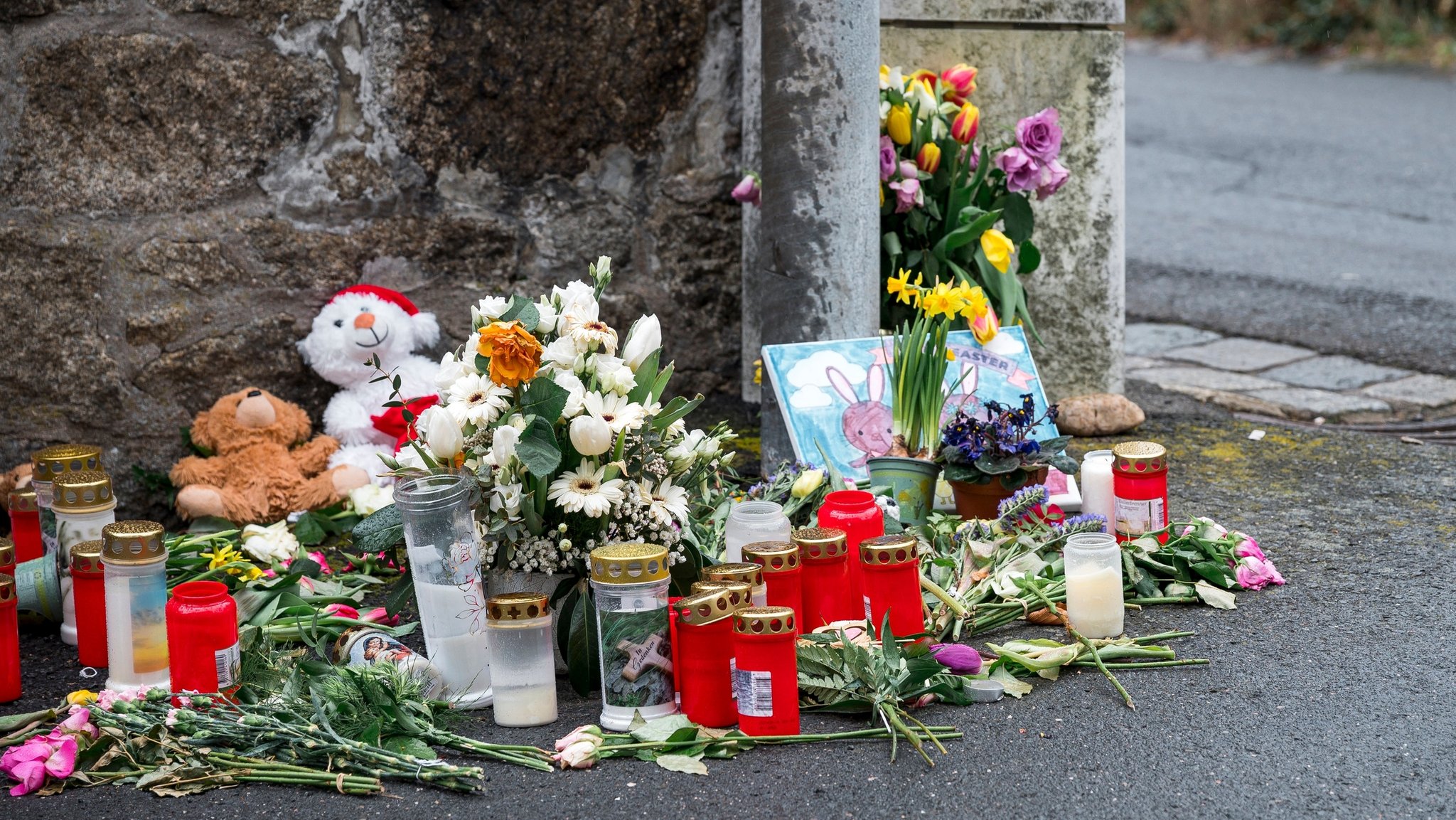 ARCHIV - 12.04.2023, Bayern, Wunsiedel: An einer Mauer vor dem Kinder- und Jugendhilfezentrum, in dem eine Zehnjährige tot aufgefunden wurde, liegen Blumen, Kuscheltiere und Kerzen. (zu dpa: «Mädchen in Kinderheim vergewaltigt - Prozessbeginn im Februar») Foto: Daniel Vogl/dpa +++ dpa-Bildfunk +++