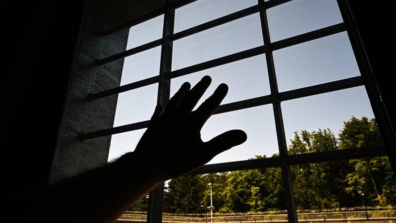Ein Mann hält in einer Einzelzelle seine Hand ans Fenster. (Symbolbild)