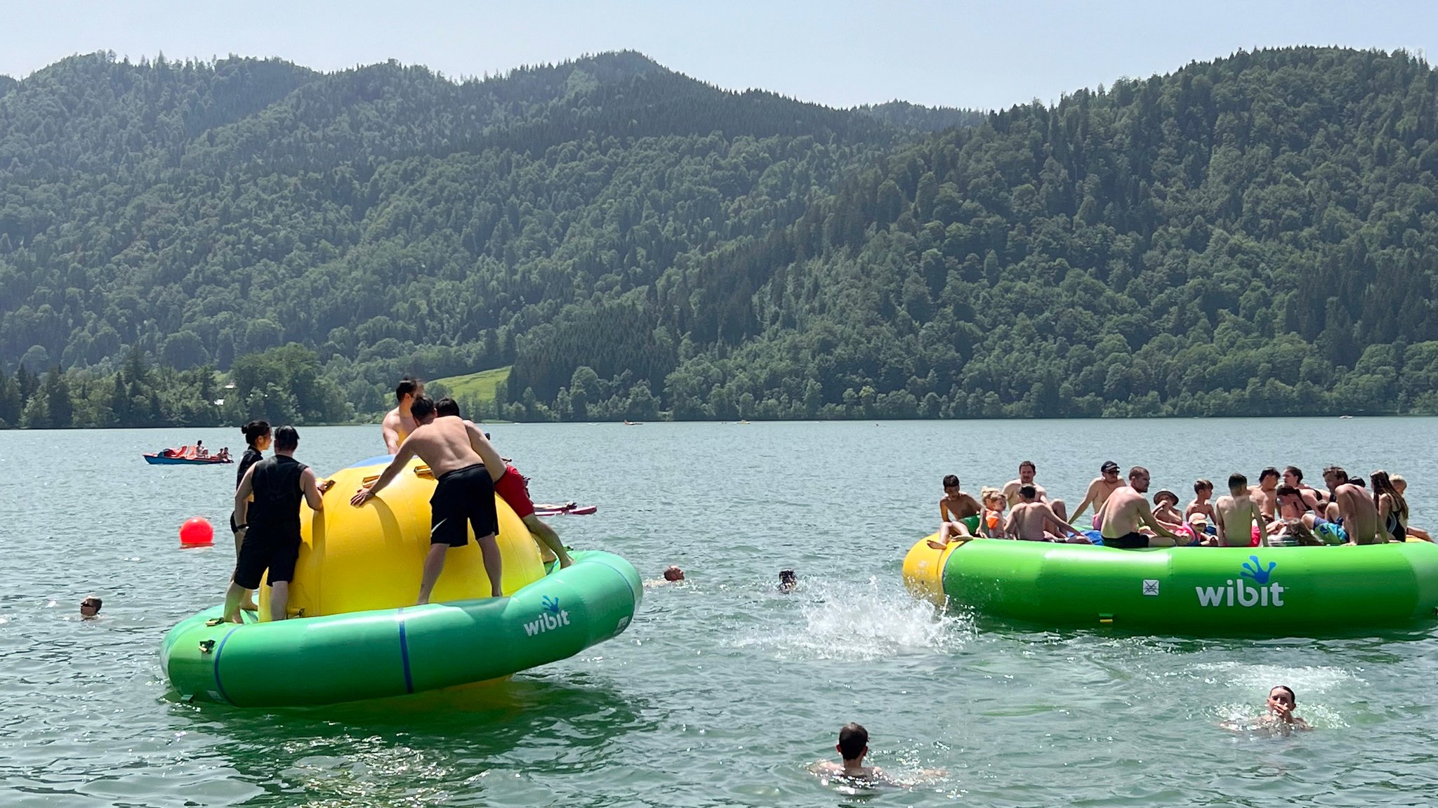 Menschen auf Badeinseln auf einem See, der von bewaldeten Bergen umgeben ist