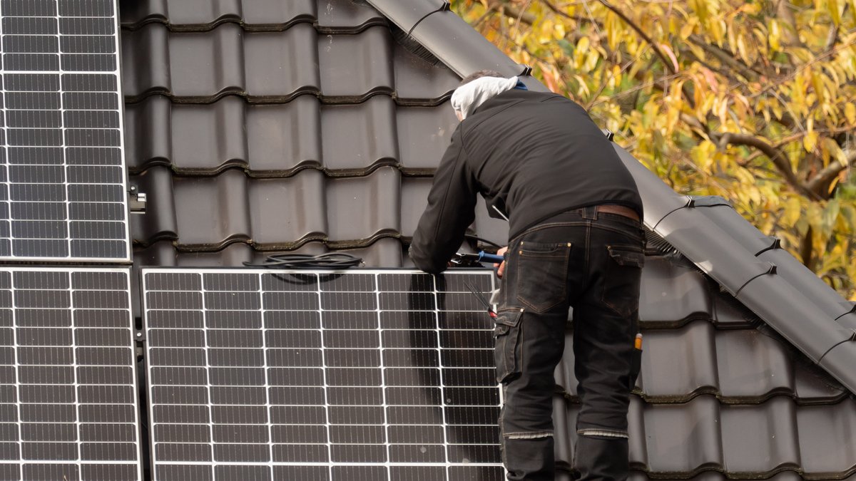 Ein Handwerker steht auf dem Dach eines Einfamilienhauses und arbeitet an einem Solarmodul.