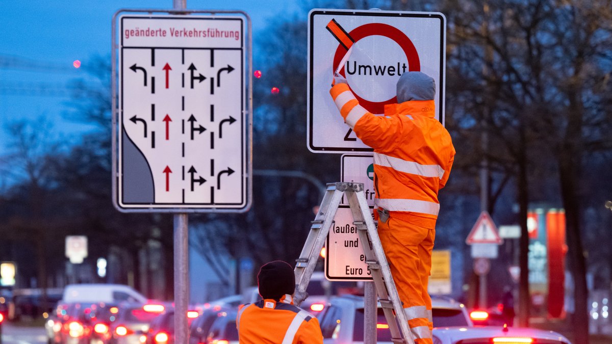 01.02.2023, Bayern, München: Arbeiter entfernen einen roten Klebestreifen von einem Schild mit der Aufschrift «Umwelt Zone» und «Diesel (außer Lieferverkehr und Anwohner) erst ab Euro 5/V». 