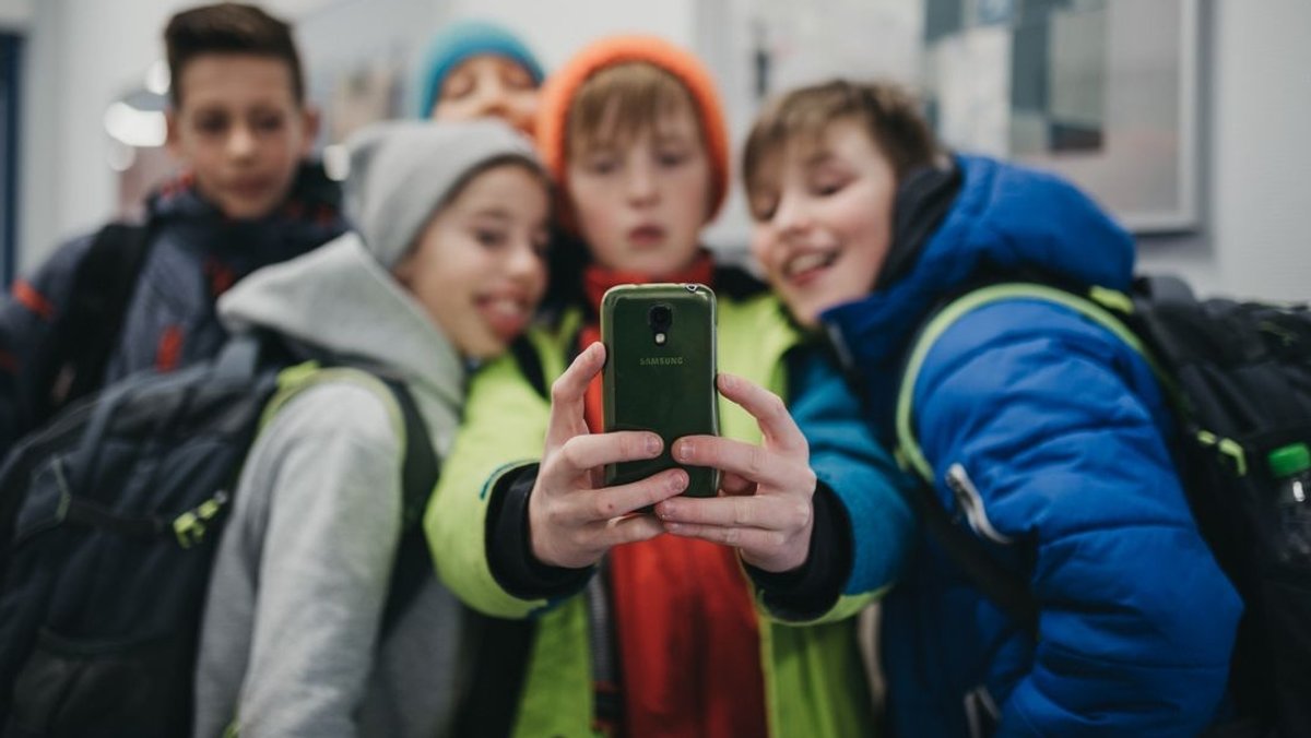 Drei Schüler schauen zusammen auf ein Smartphone (Symbolbild)