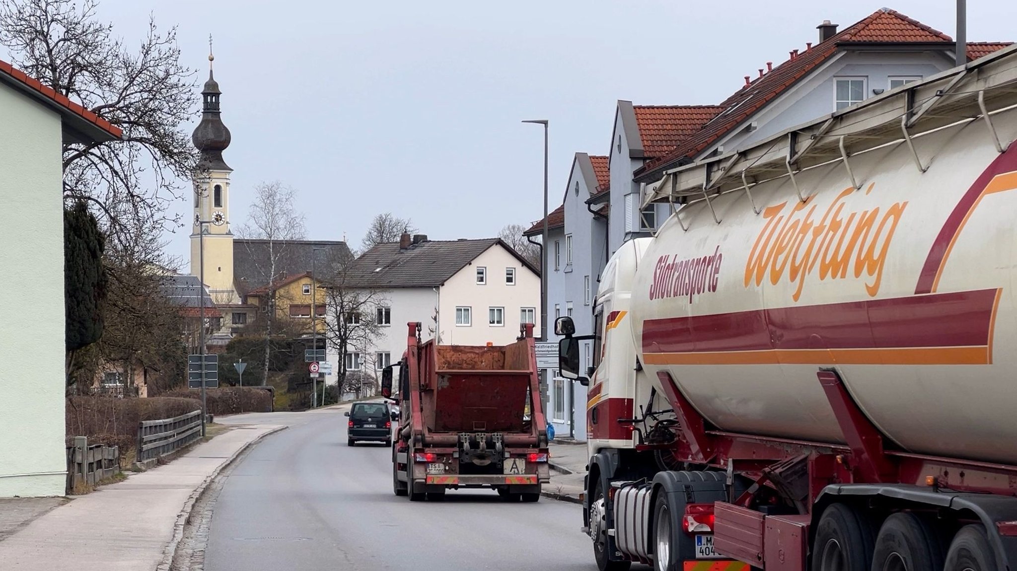 Zwei Lkw und ein Pkw fahren durch den Ortskern von Altenmarkt. 