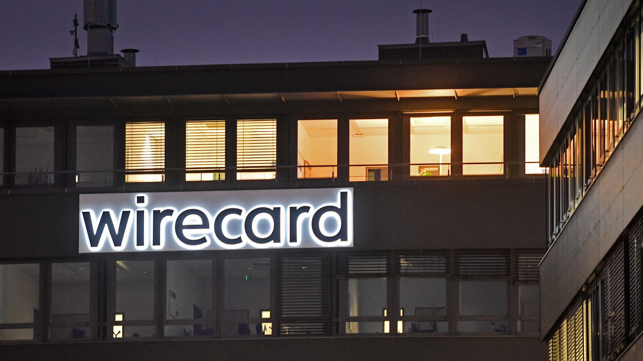 Die Fassade des Firmensitzes von Wirecard im Dunkeln, an der Fassade befestigt das beleuchtete Logo mit dem Firmennamen. Ein globales Netzwerk soll unter anderem Wirecard für massenhaften Kreditkarten-Betrug genutzt haben.