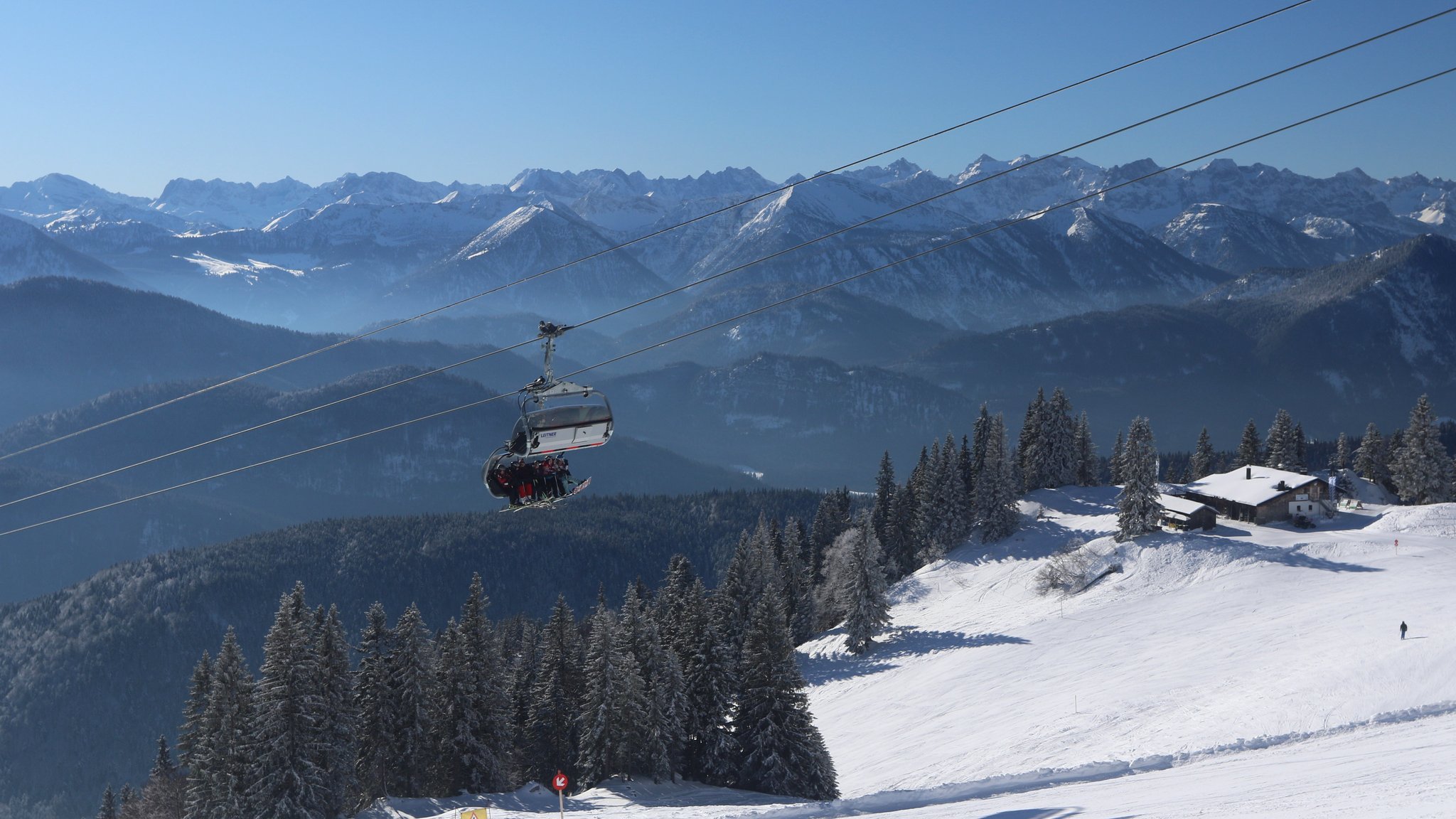 Über eine beschneite Skipiste fährt eine Gondel mit Skifahrern, im Hintergrund das Karwendel-Gebirge.