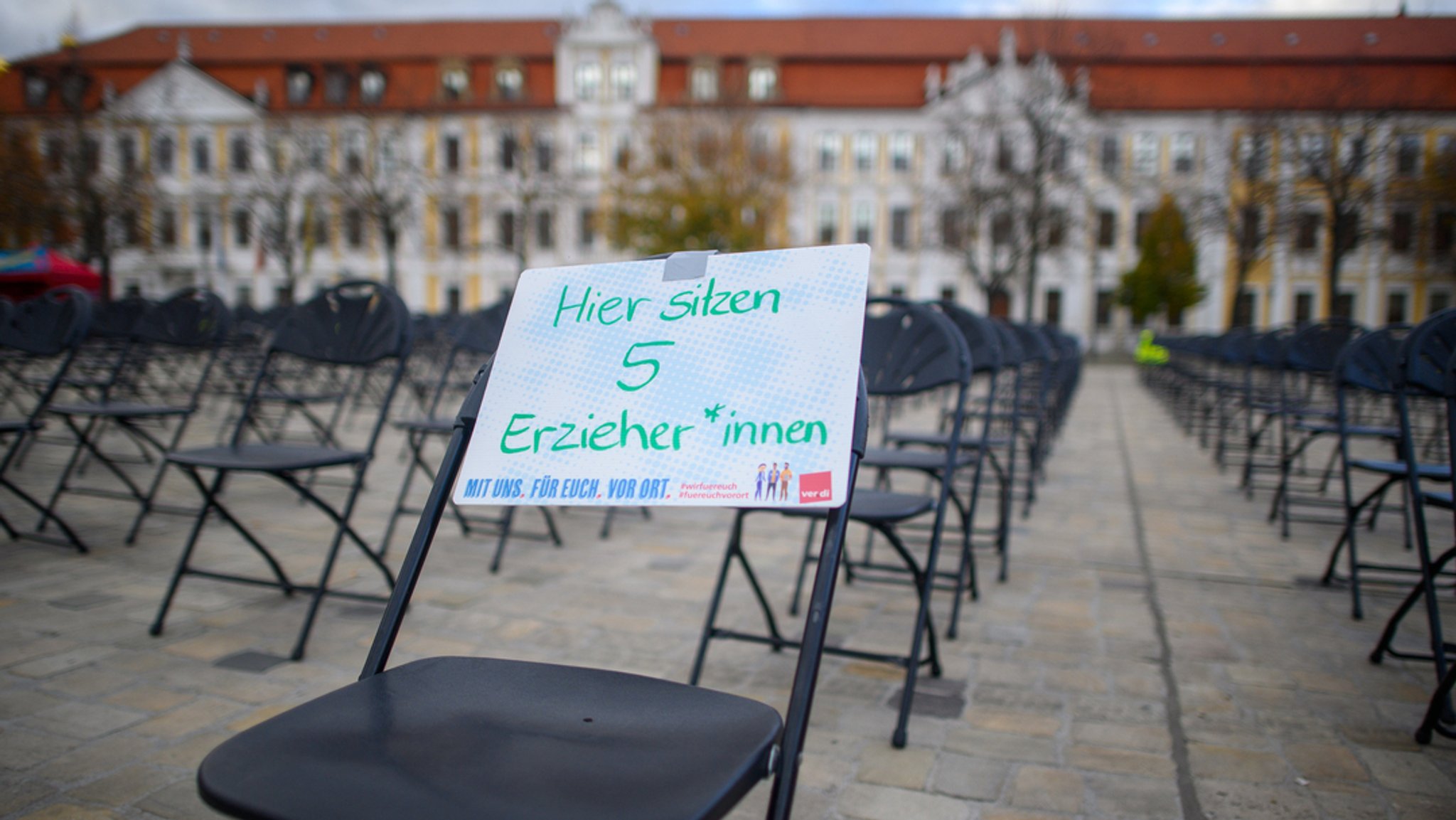 Archiv: 19.10.2022, Sachsen-Anhalt, Magdeburg: "Hier sitzen fünf Erzieher*innen" steht auf einem Schild, das auf dem Domplatz an einem Stuhl festgemacht ist. Im Hintergrund ist der Landtag zu sehen. Die Gewerkschaft Verdi hat hier insgesamt 800 Stühle bei einer Protestaktion aufgestellt. Jeder Stuhl soll dabei für 5 fehlende Erzieher und Erzieherinnen stehen. Laut Gewerkschaft fehlen 4.000 Kräfte an kommunalen Kitas und Horten in Sachsen-Anhalt.