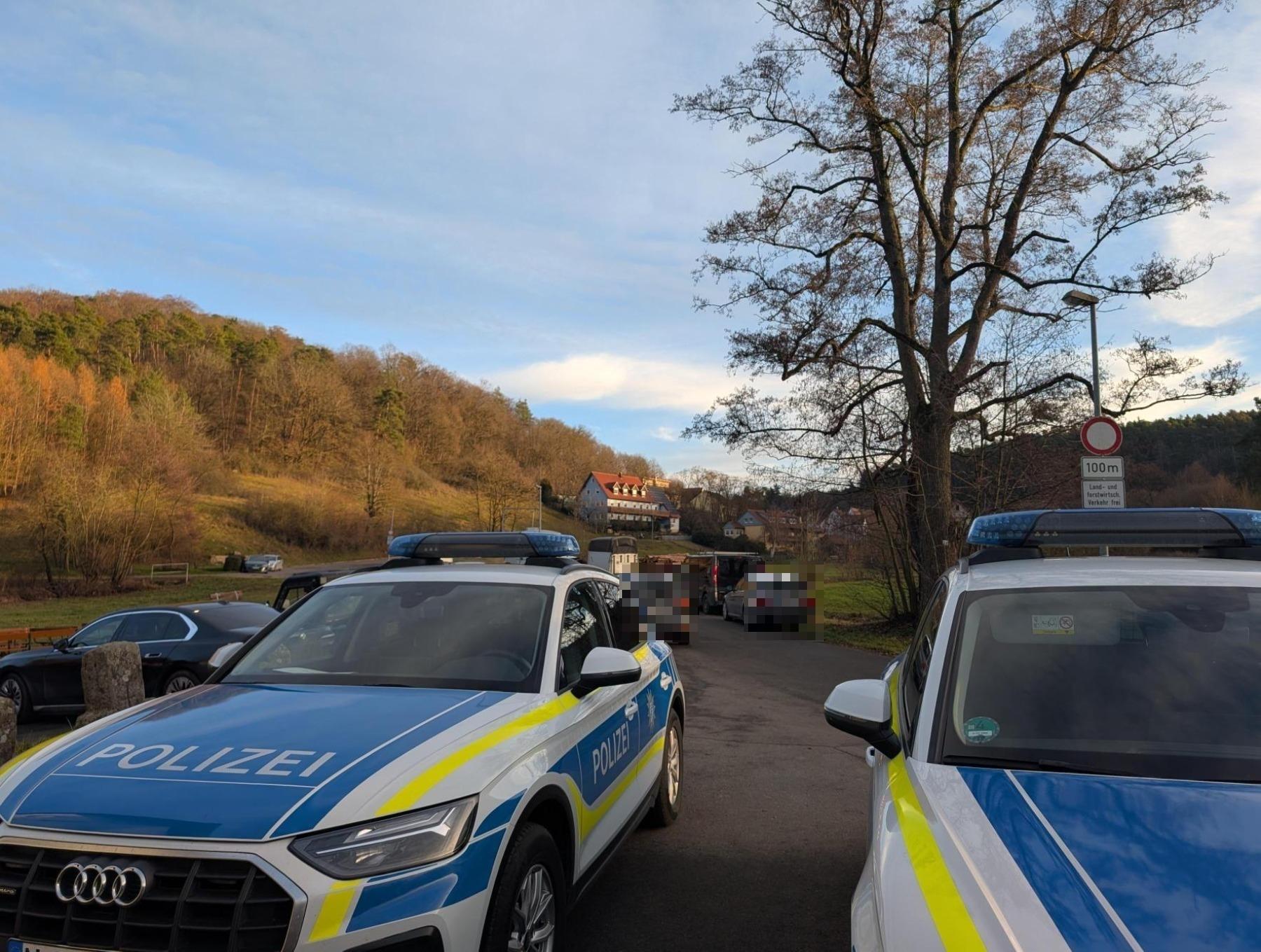 Einsatzfahrzeuge der Polizei stehen auf einer Straße. Dahinter sind weitere Pkw zu sehen. Im Hintergrund ist eine Straße zu sehen die nach Altschauerberg führt. 