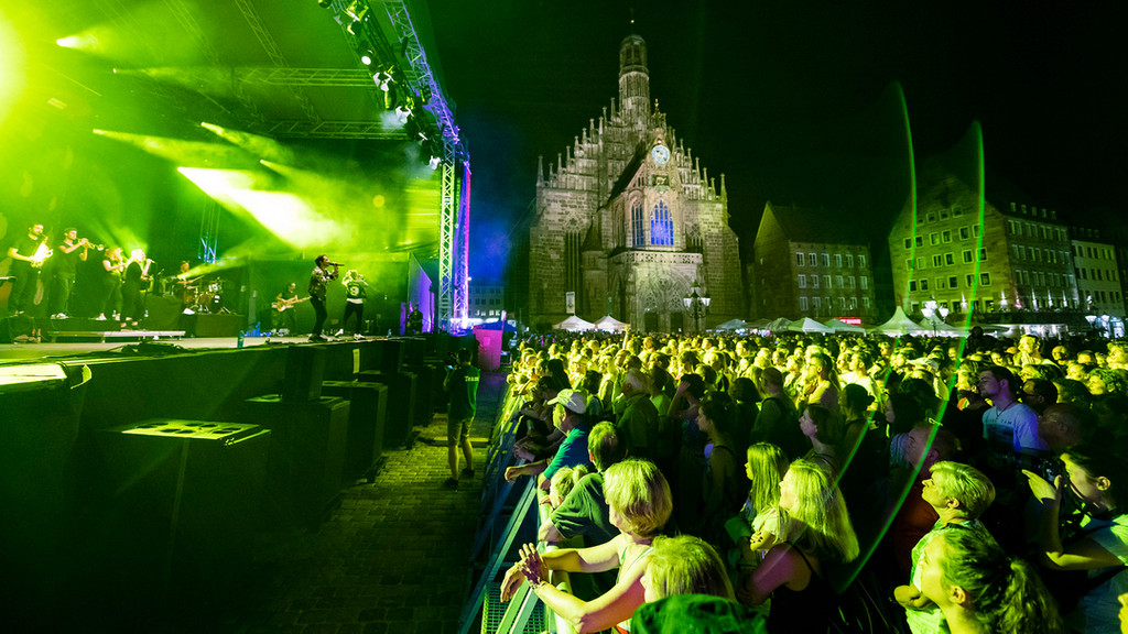 Menschen vor einer in grünes Licht getauchten Bühne auf dem Nürnberger Hauptmarkt.