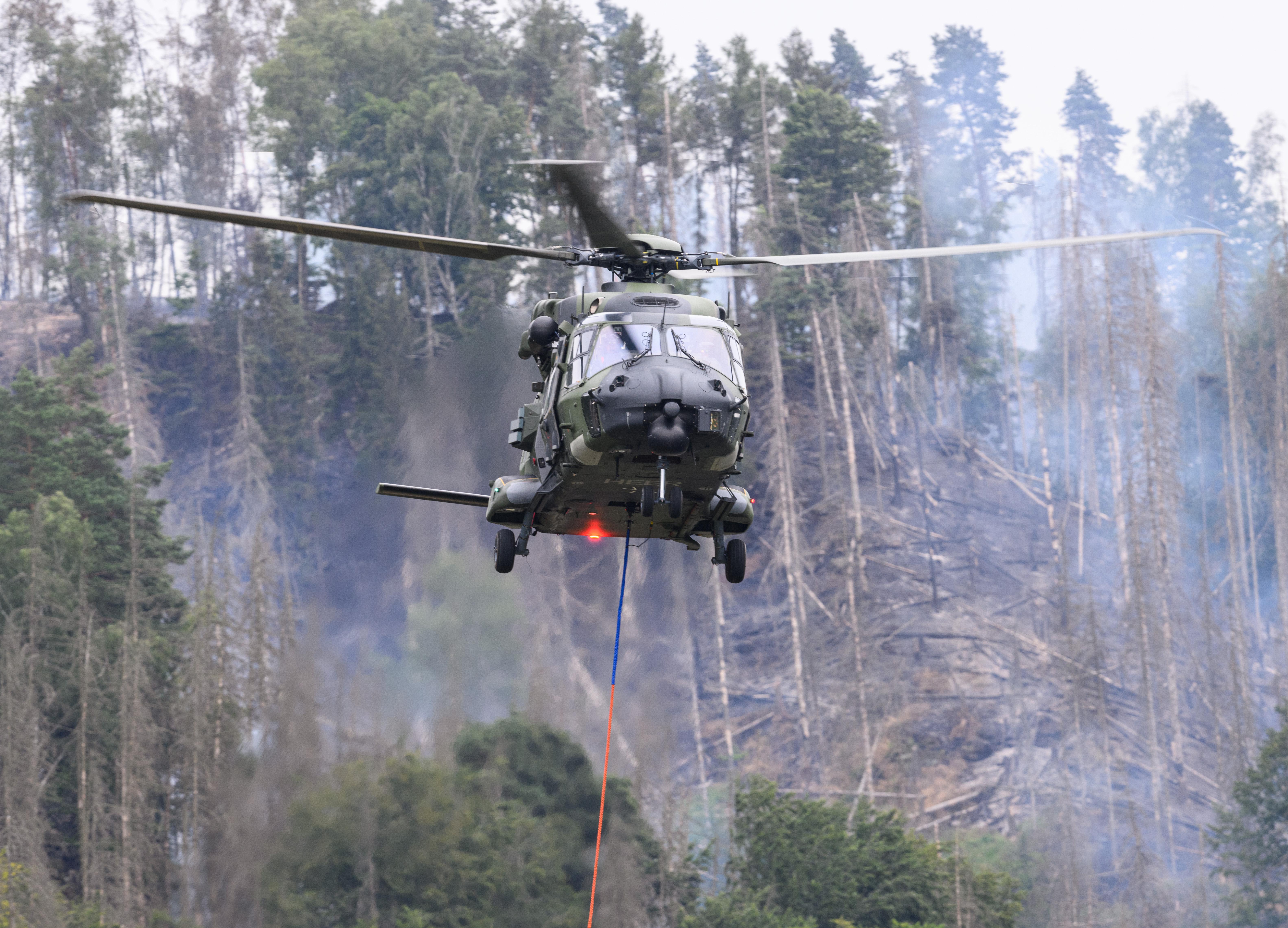 Ein Hubschrauber der Bundeswehr fliegt mit einem Löschwasser-Außenlastbehälter über einen Brand im Nationalpark Sächsische Schweiz (Archivbild).
