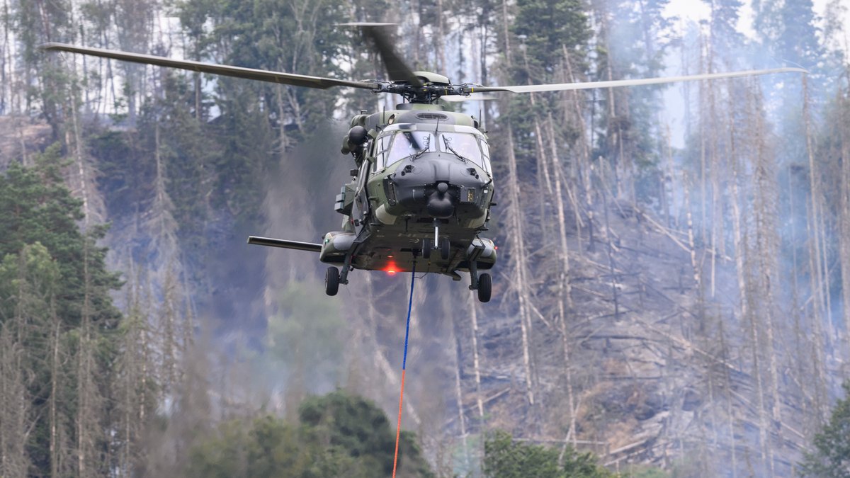 Ein Hubschrauber der Bundeswehr fliegt mit einem Löschwasser-Außenlastbehälter über einen Brand im Nationalpark Sächsische Schweiz (Archivbild).